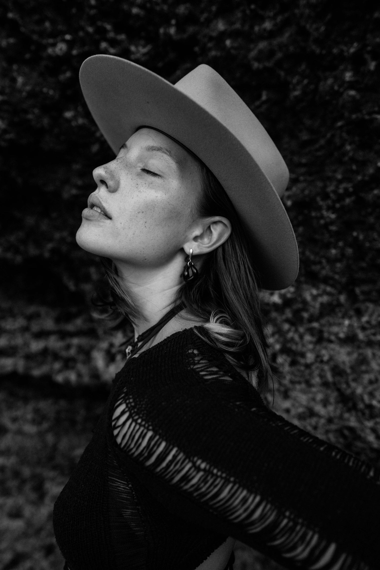 Black and white portrait of woman wearing wide-brim hat with eyes closed.