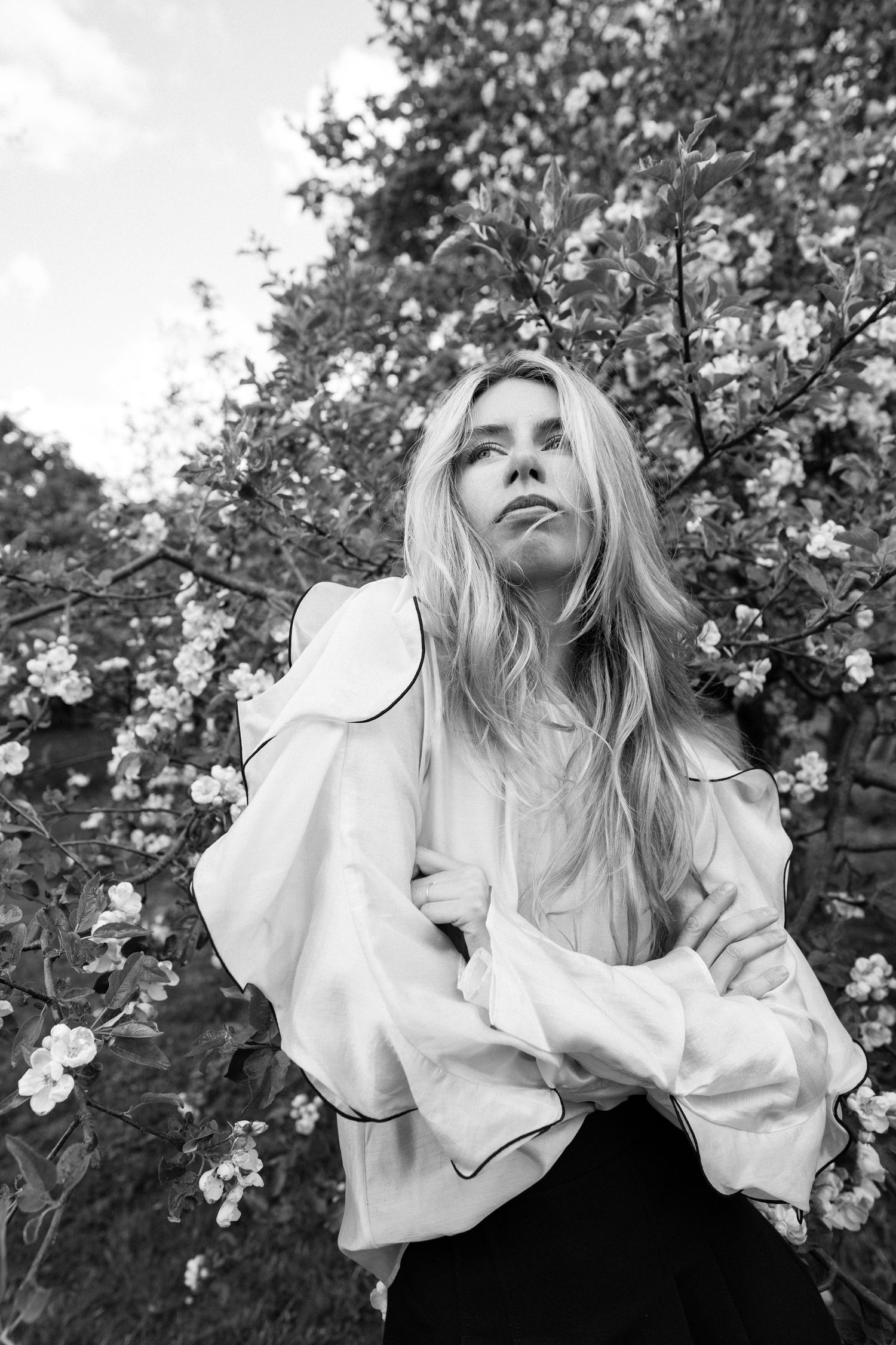 Black and white portrait of woman standing among flowering bushes with soft expression.