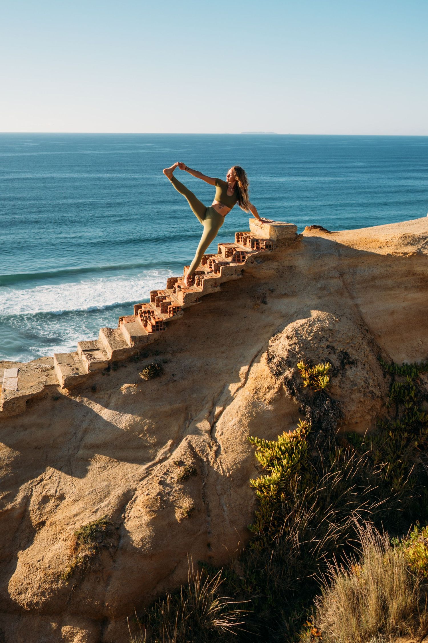 Woman ascending stone steps along rocky coastline with ocean in background.