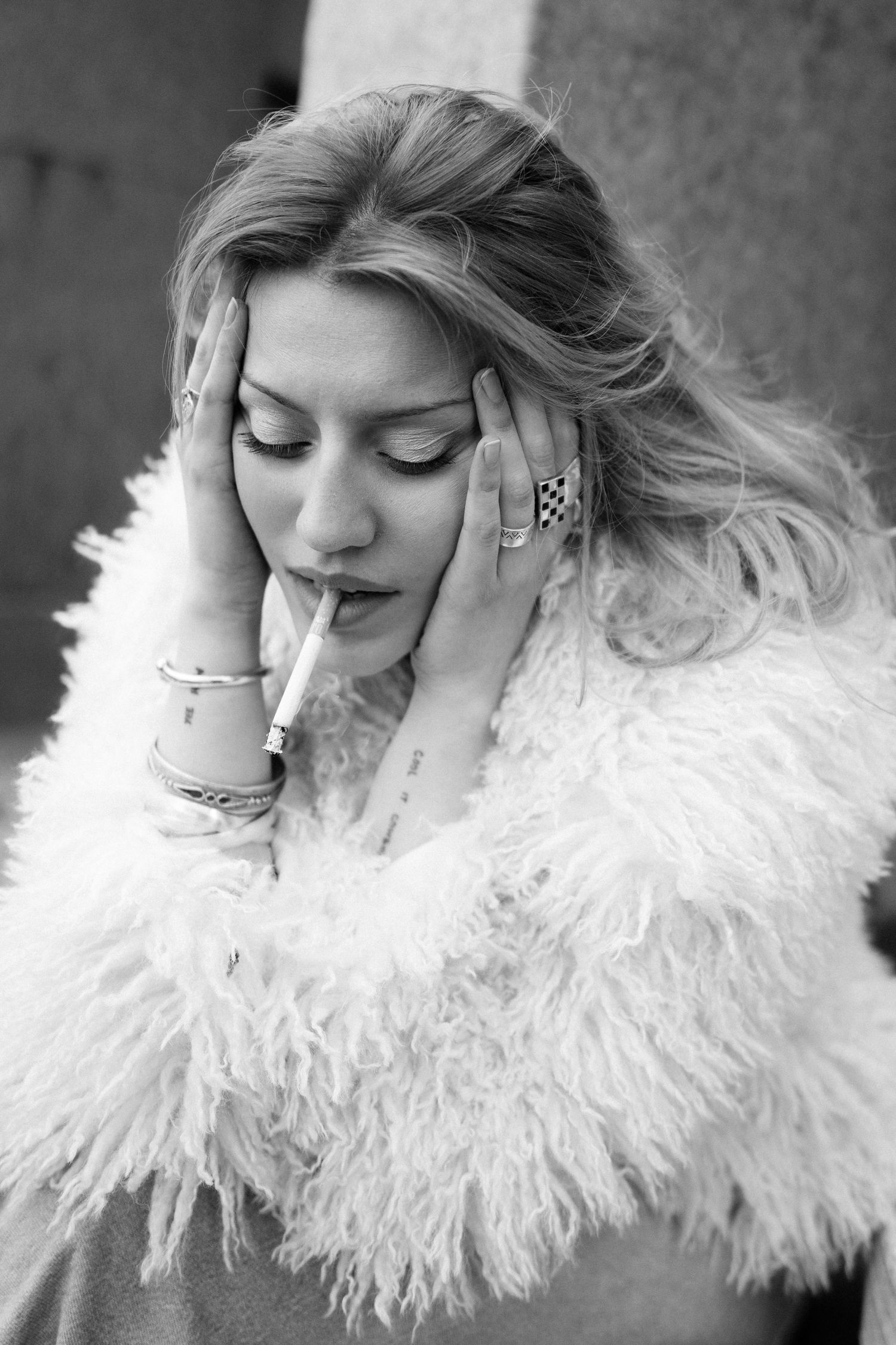 Black and white close-up portrait of woman wearing a textured jacket with soft expression smoking a cigarette