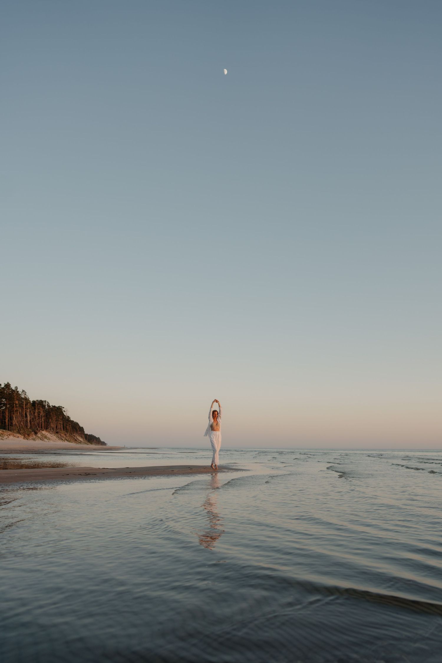 Distant figure standing on beach beneath open sky at dusk.