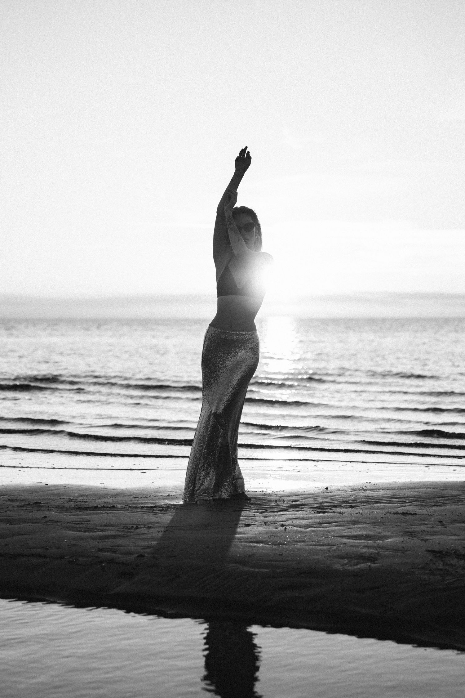 Black and white silhouette of woman raising her arm by the ocean shoreline