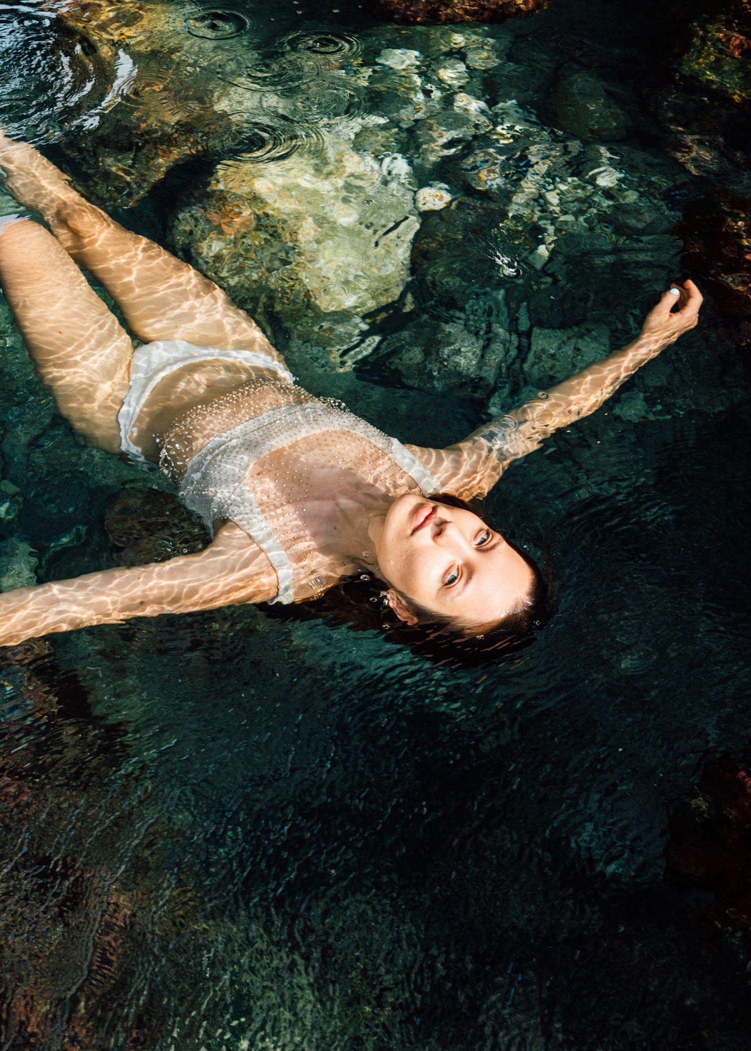 Woman floating on her back in clear shallow water viewed from above.