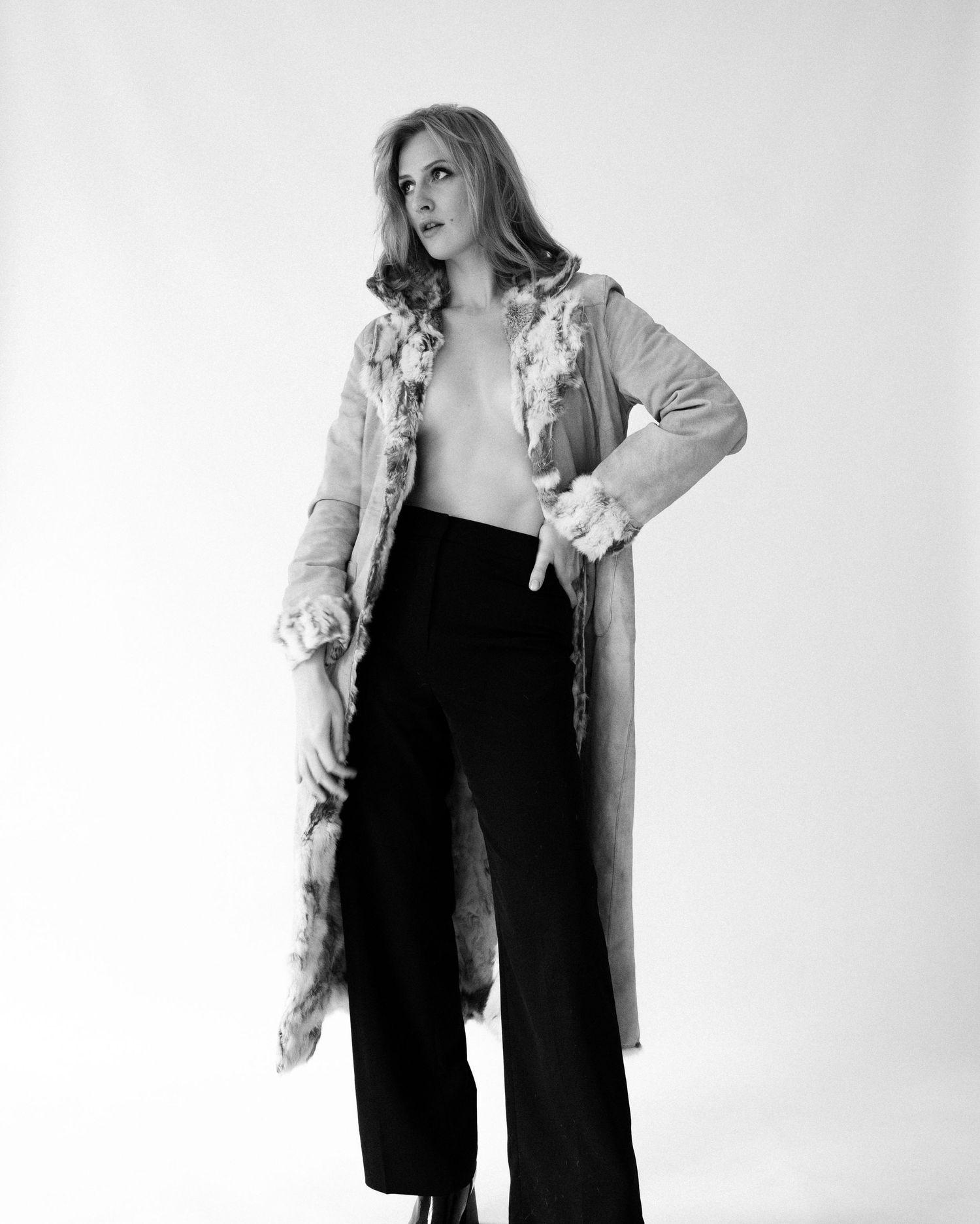 Black and white fashion portrait of woman wearing long coat and wide-leg trousers.