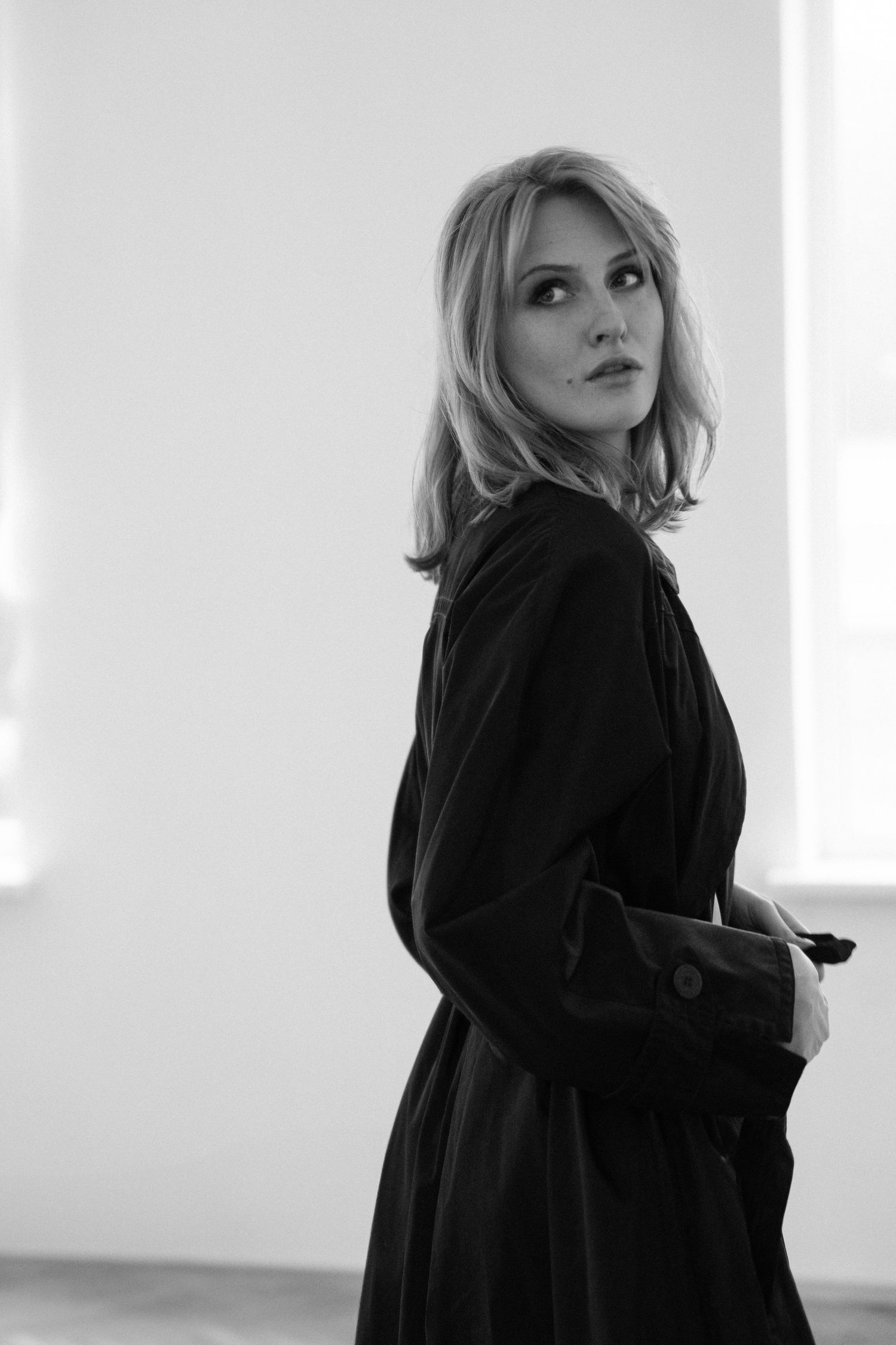 Black and white portrait of woman turning toward camera in minimal interior space.