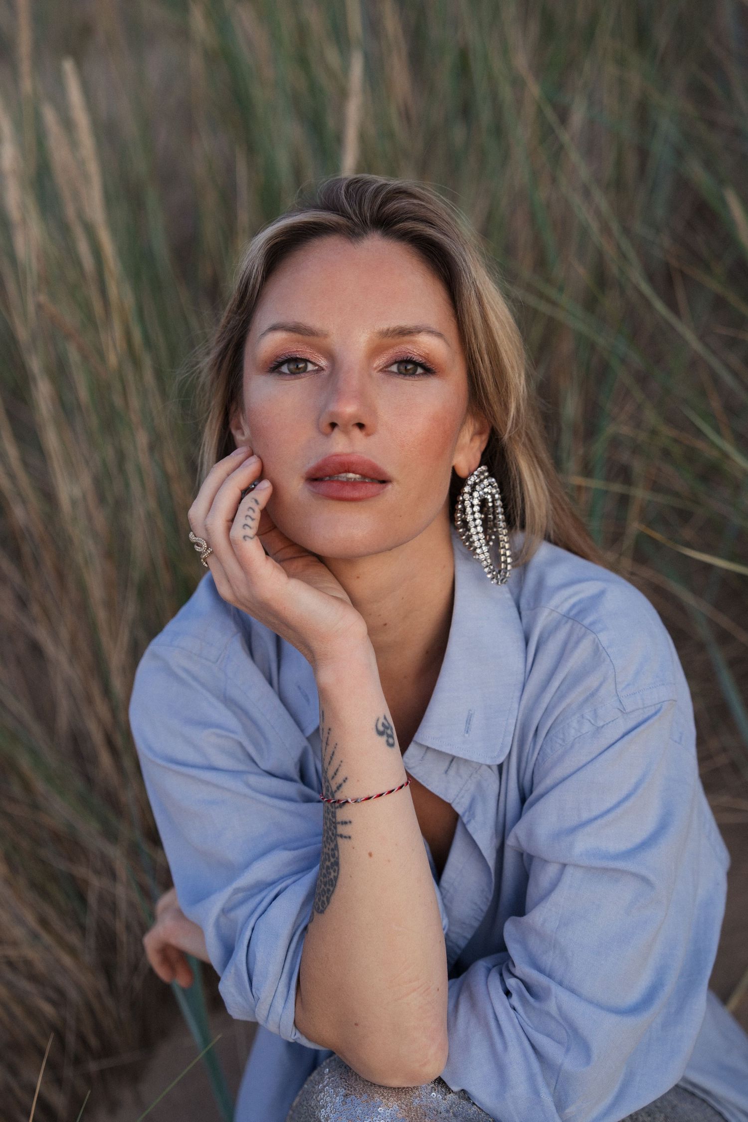 Close-up portrait of woman seated in tall grass wearing light blue shirt.