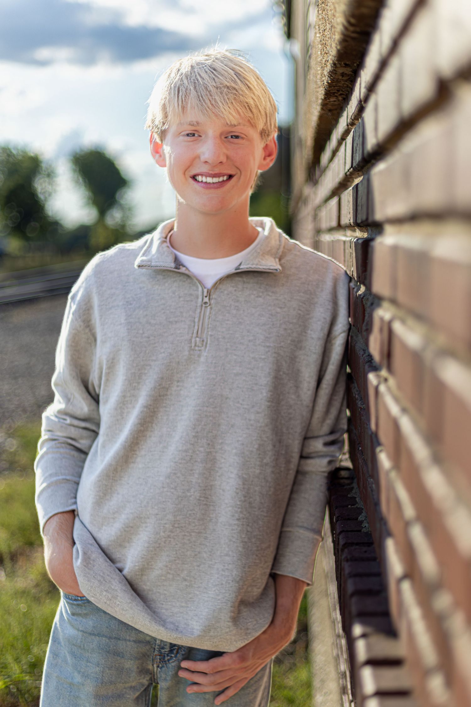 Kansas City portrait photography. Professional senior photo of a young man leaning against a brick wall and smiling, backlit.