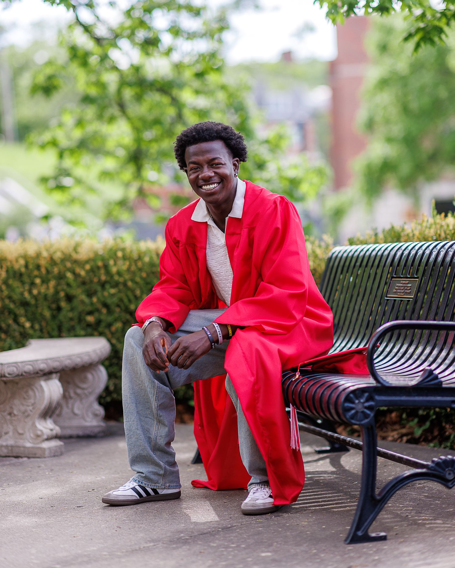 Cap and gown photo of a young man seated on a bench at Park University in Parkville | Kansas City Northland Portrait Photographer