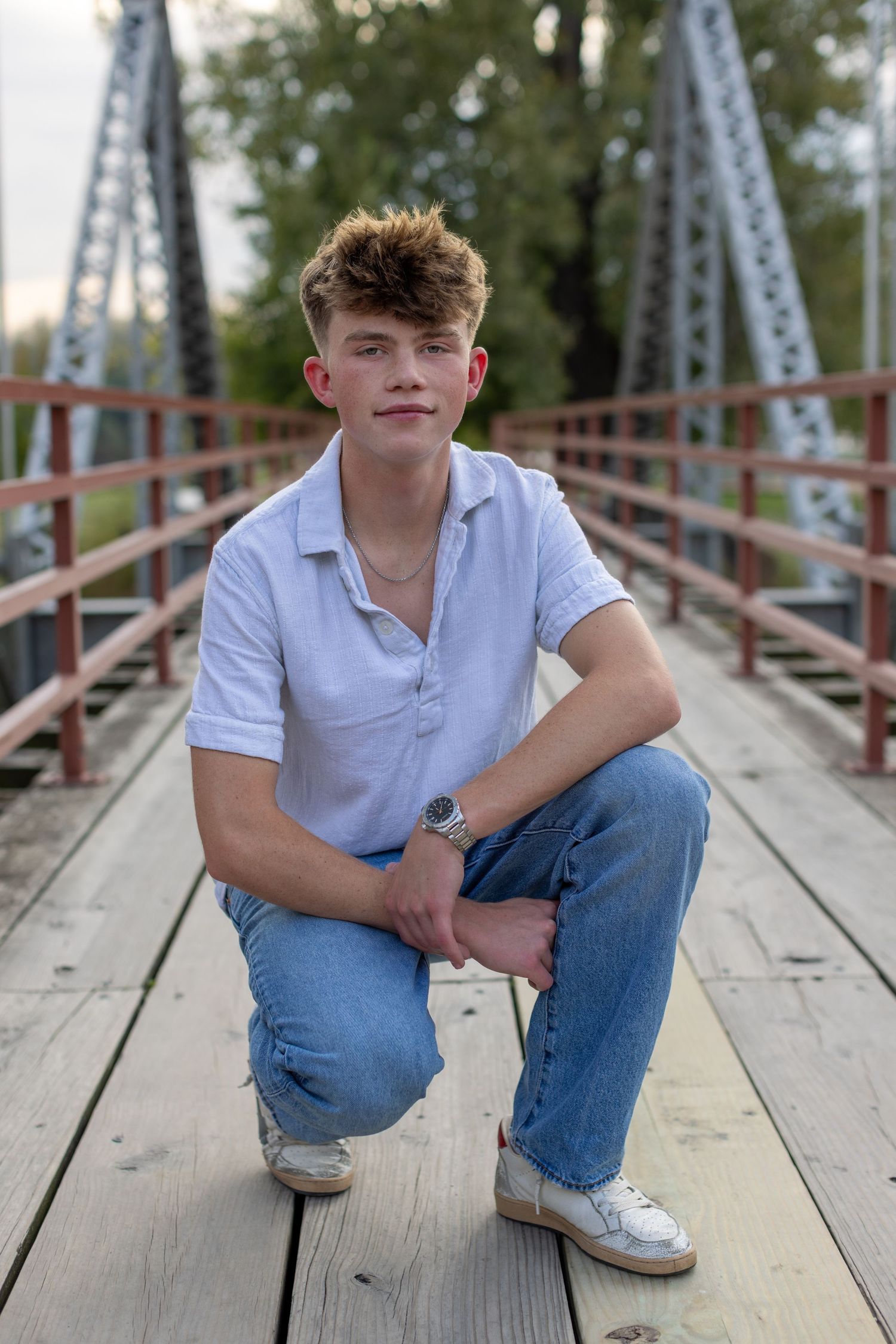 Graduation photo of a young man kneeling on the bridge at English Landing Park in Parkville | Kansas City Northland Portrait Photographer