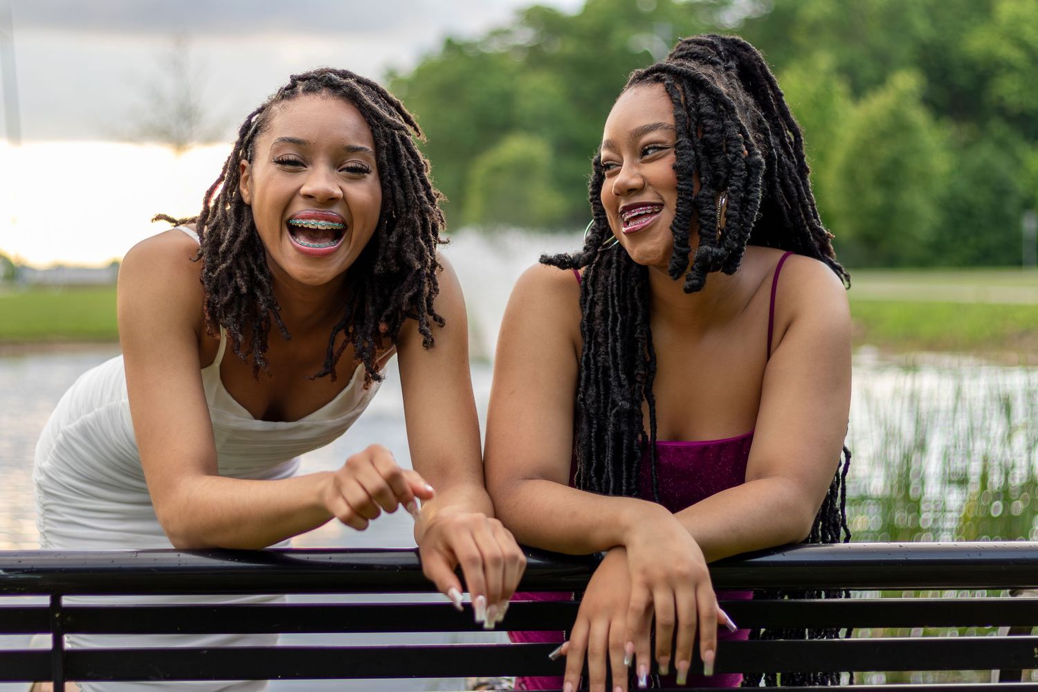 Graduation photo of sisters laughing while leaning on a park bench at the Riverside Waterfall | Kansas City Northland Portrait Photographer