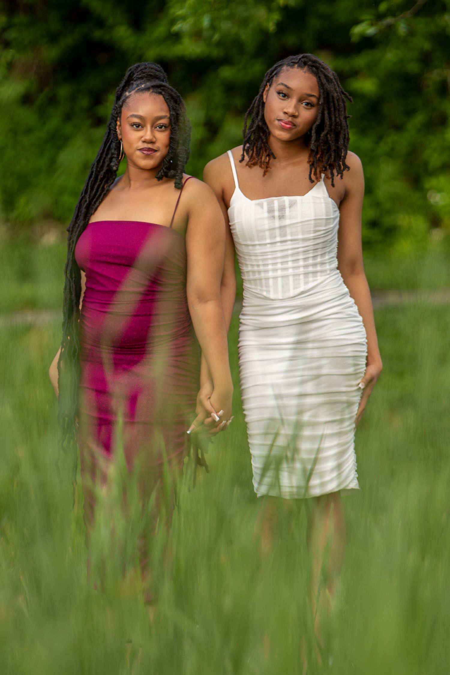 KC portrait photography. Professional senior photo of two sisters wearing dresses and holding hands in a grassy field.