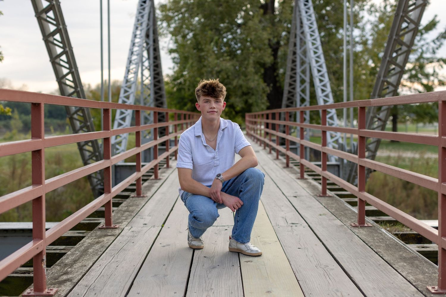 Kansas City portrait photography. Professional senior photo of a young man crouching on a trestle bridge.