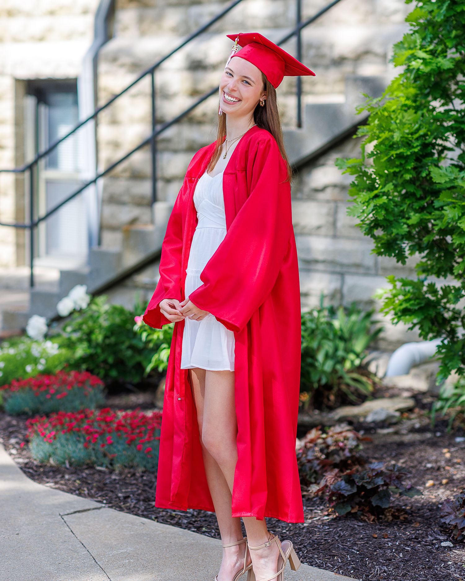Cap and gown photo of a young lady standing near a stone building at Park U in Parkville | Kansas City Northland Portrait Photographer