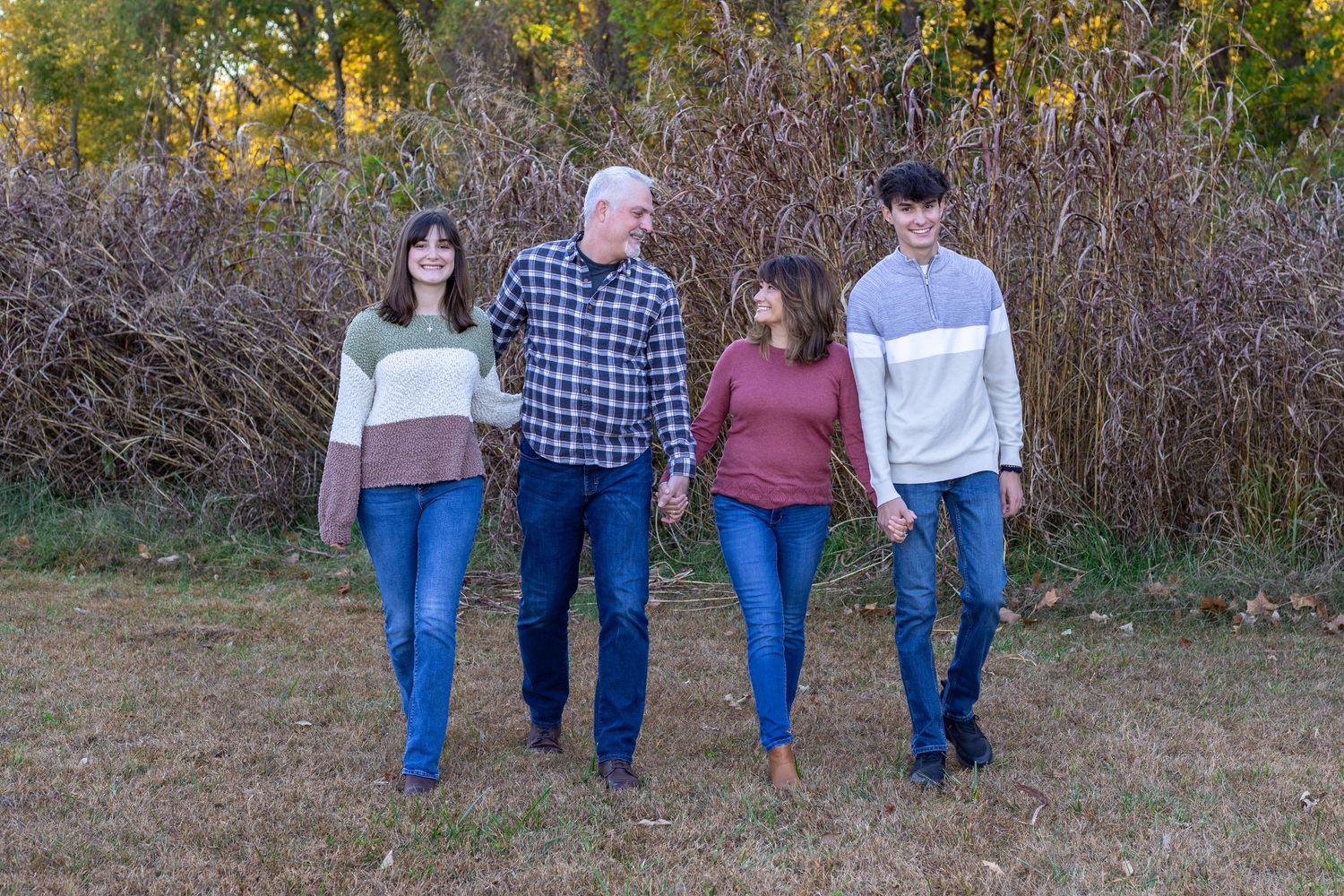 Kansas City portrait photography. Professional photo of a family of four holding hands and walking toward camera in a park-like setting.