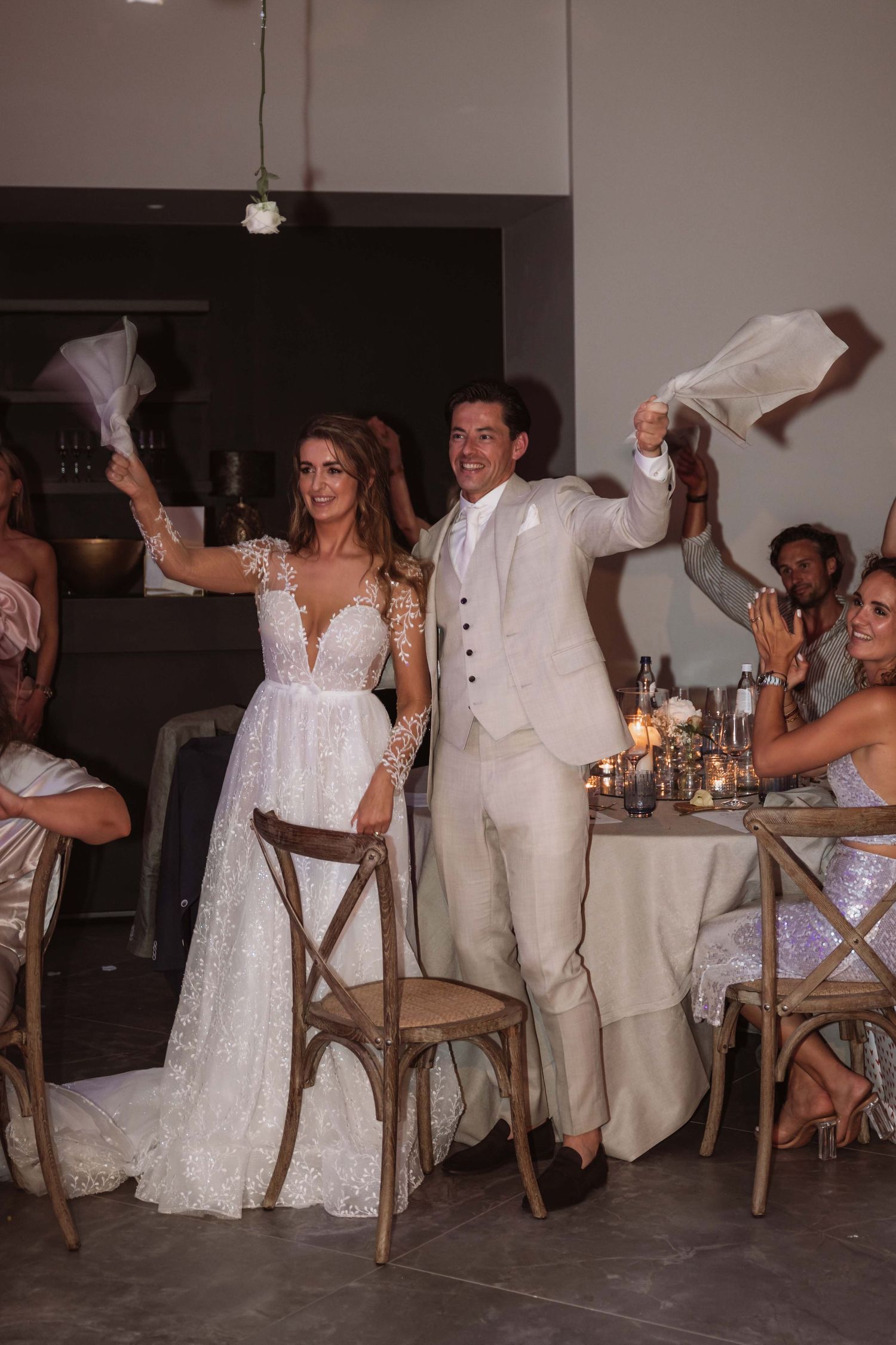 Wedding party members in white attire dance and celebrate during a joyful reception sequence.