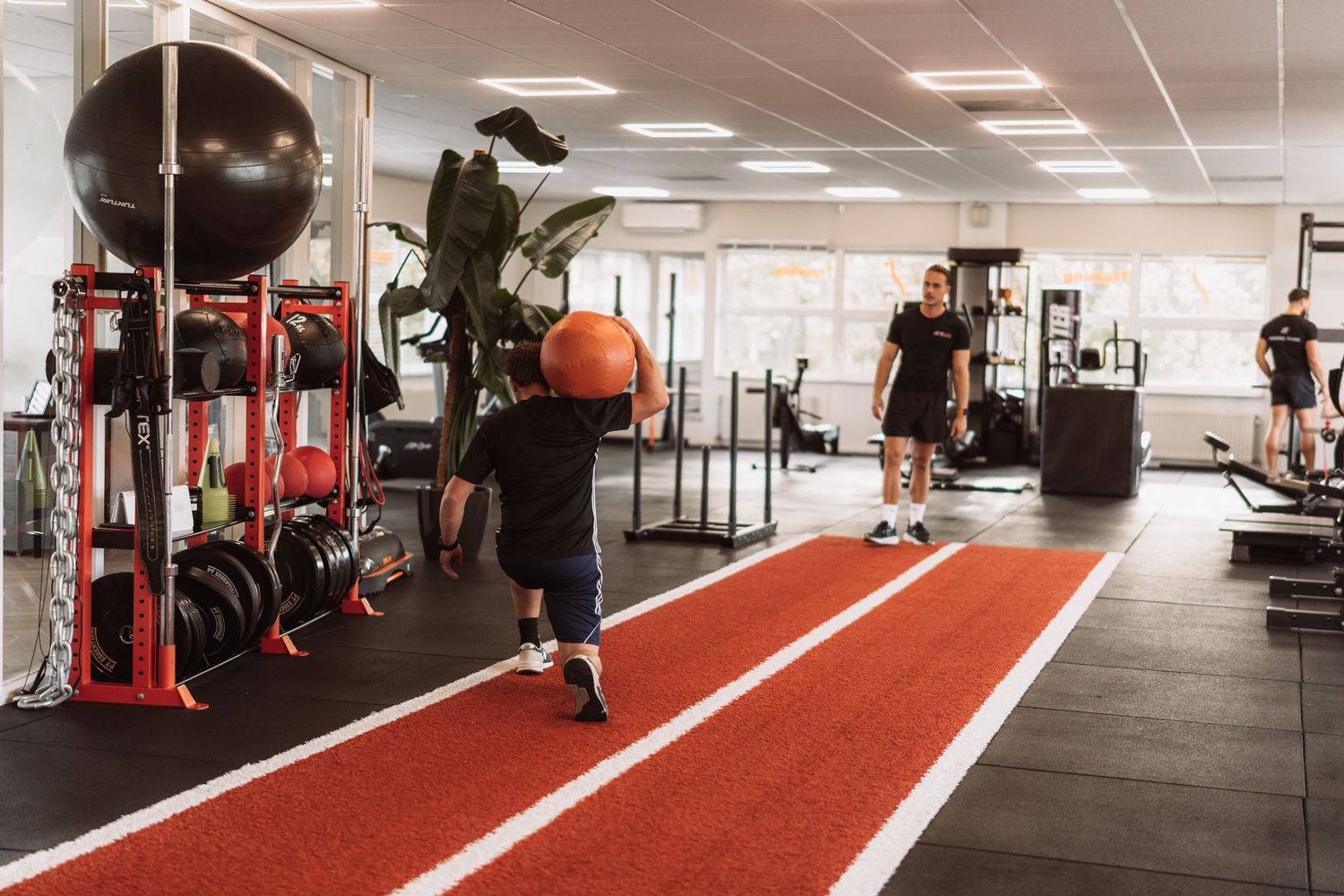Modern fitness facility interior with red turf track lanes and exercise equipment along white walls.