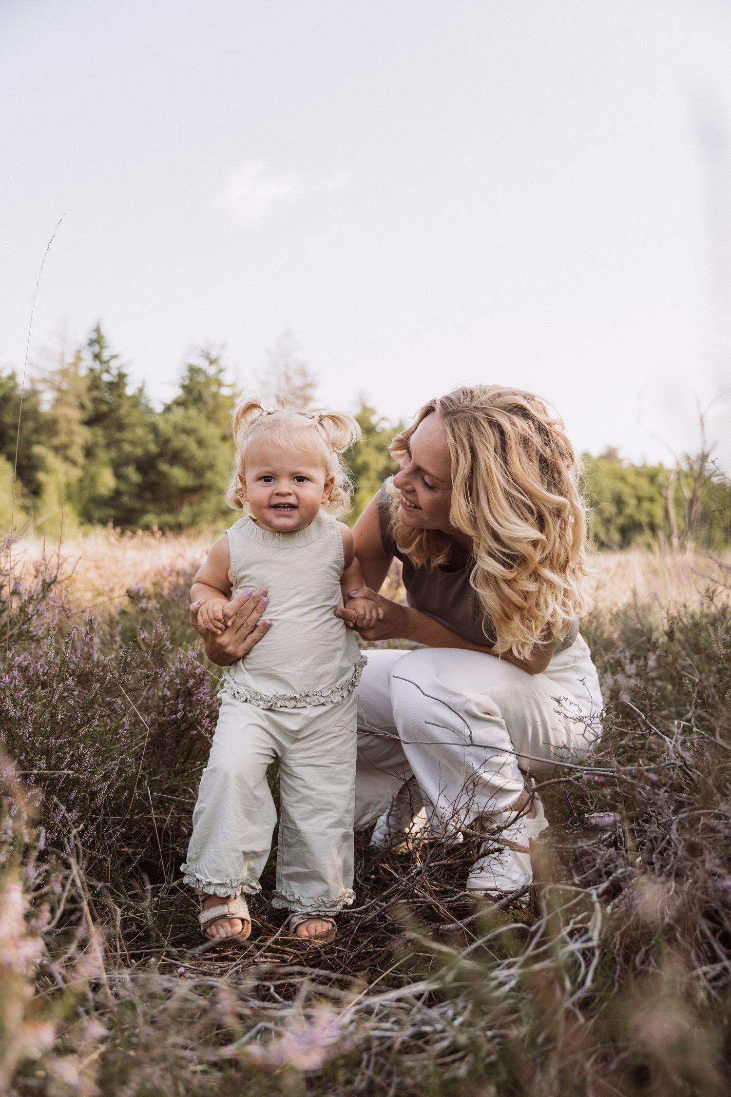 Parent and child playing together in a field of tall grass during golden hour.