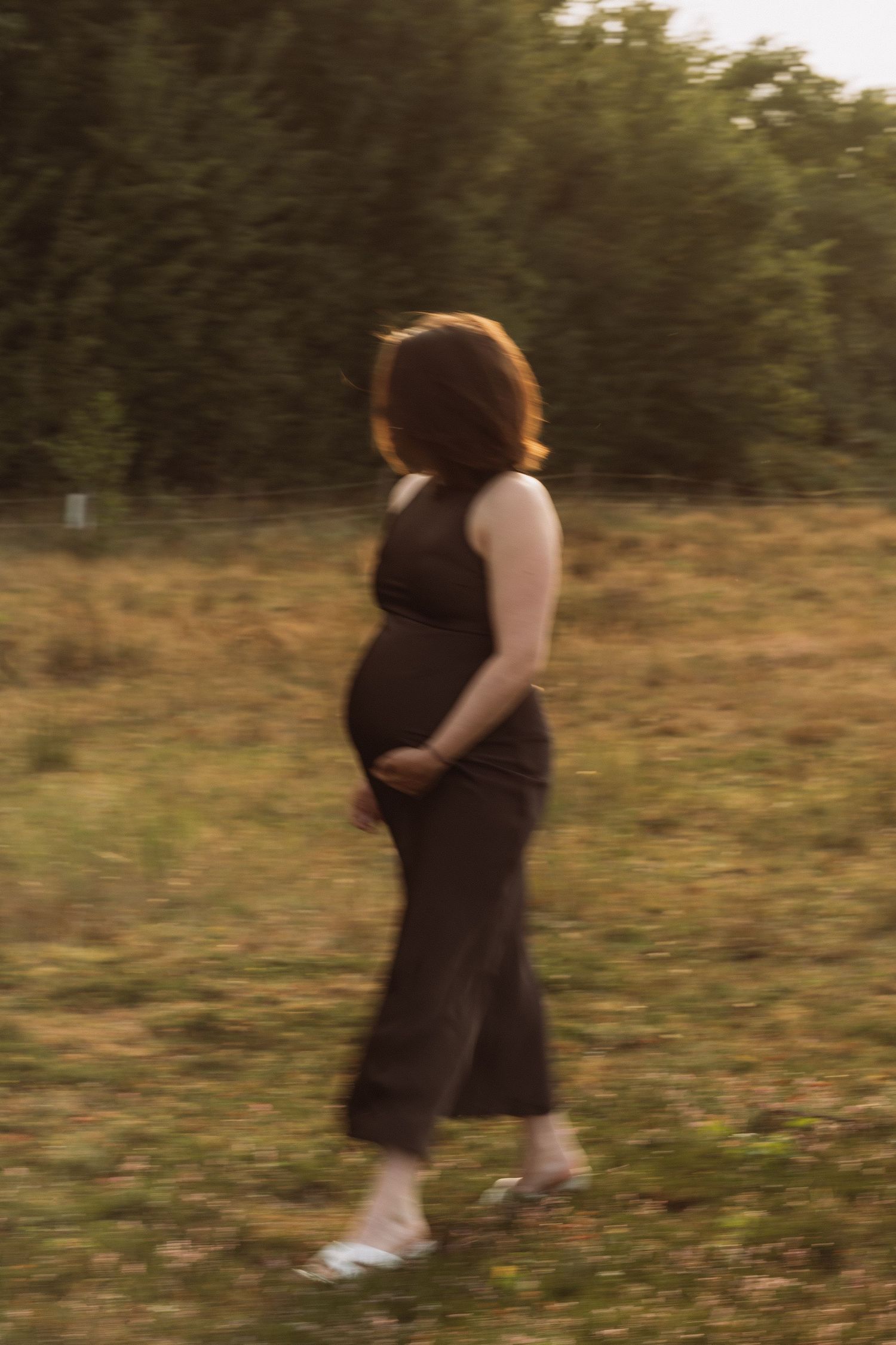 A silhouette stands in a field during golden hour wearing a flowing black dress.