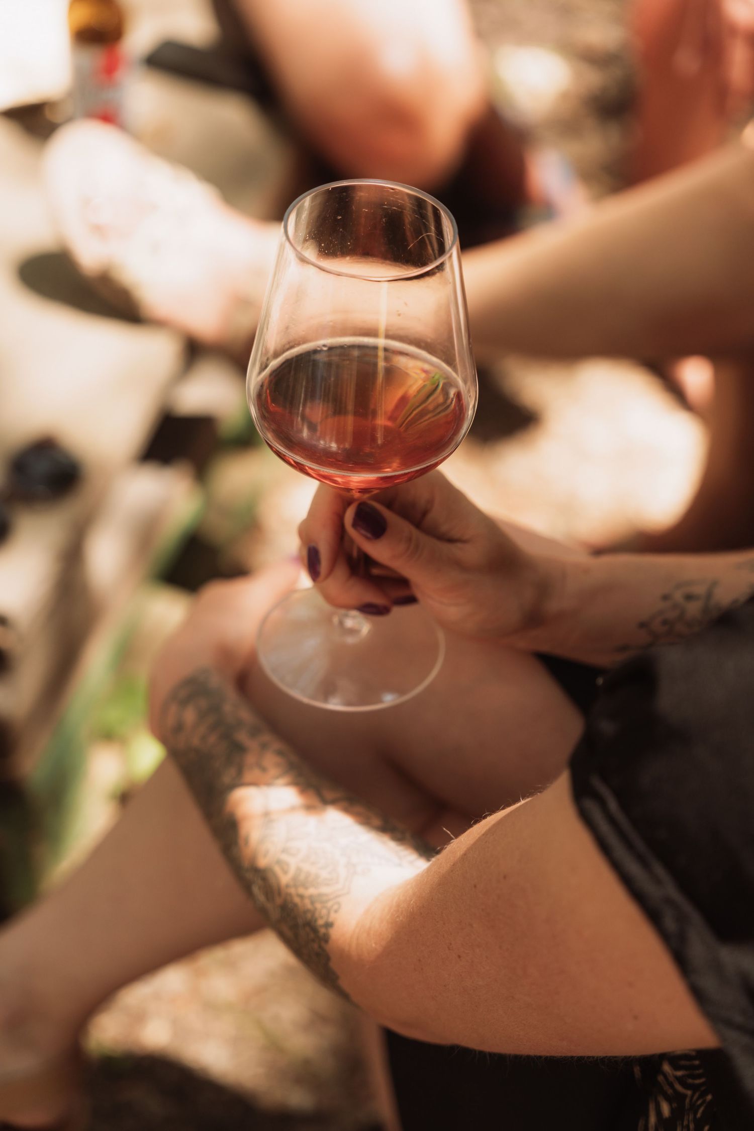 Multiple hands holding wine glasses with red wine during a tasting event in warm lighting.