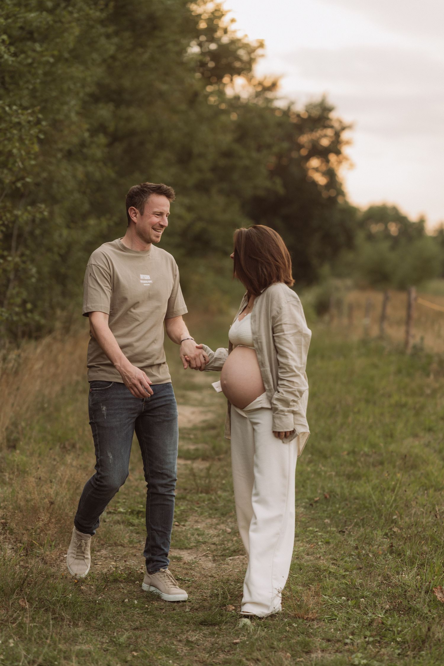 Expectant couple walking and interacting in a field during golden hour.