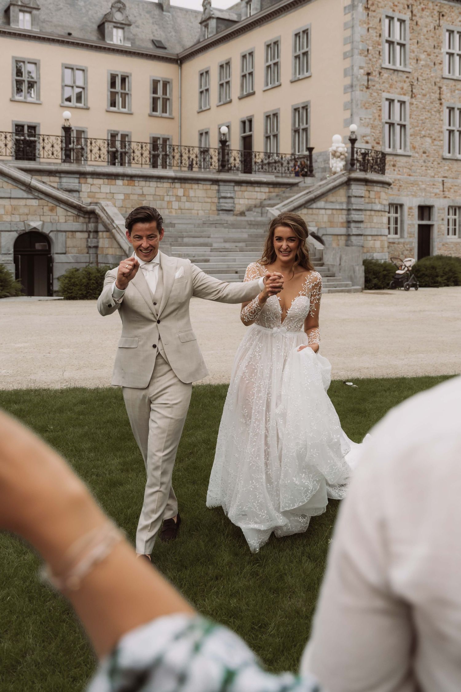 A joyful couple celebrates their wedding day on the lawn of a grand historic stone building.