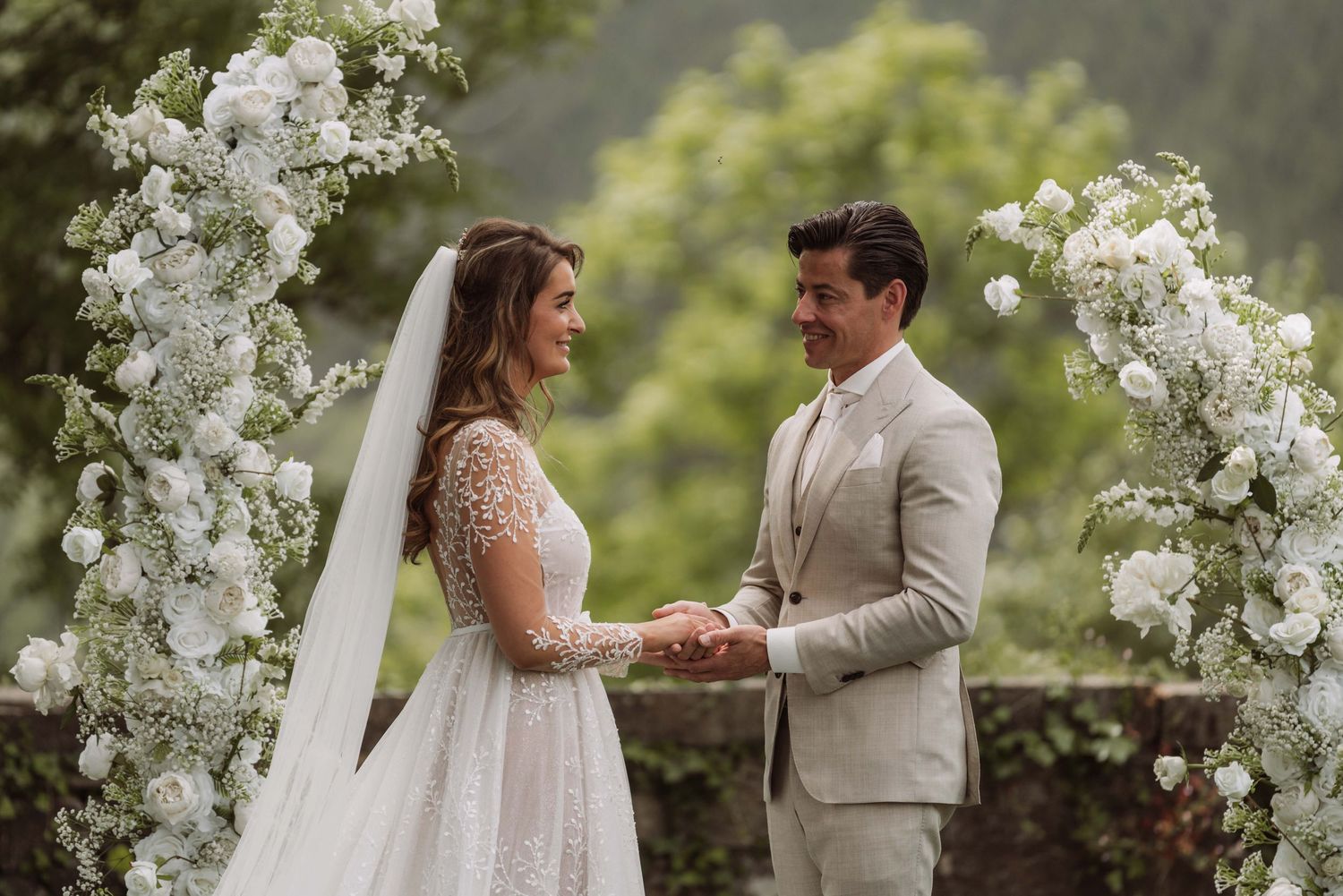 A couple shares an intimate moment during their outdoor garden wedding ceremony surrounded by white floral arrangements.