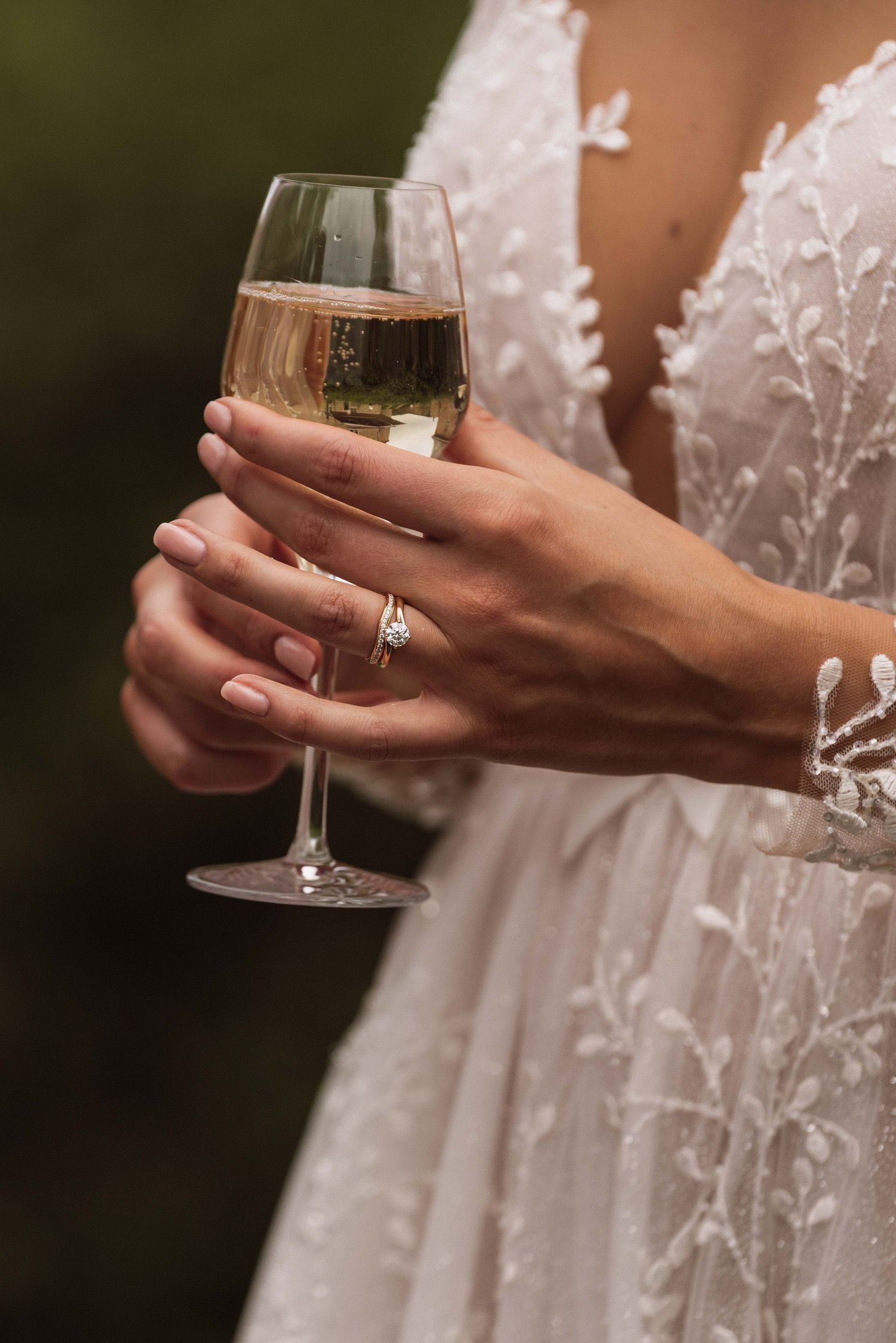 Close-up shots of hands holding a champagne glass while wearing a delicate white lace dress and engagement ring.