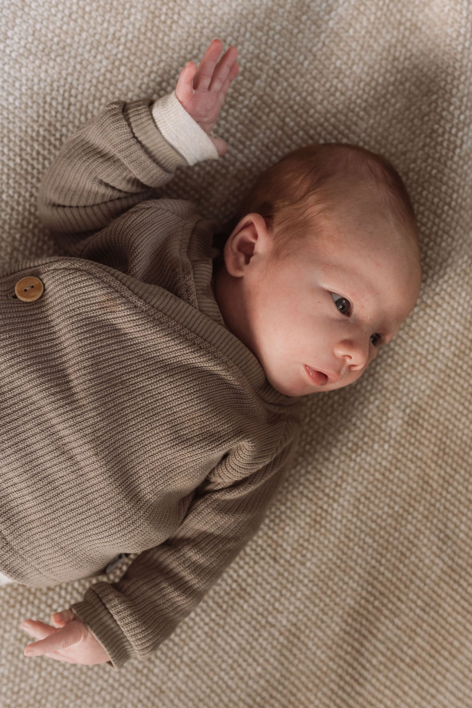 Baby wearing knit sweater lying on textured beige fabric.