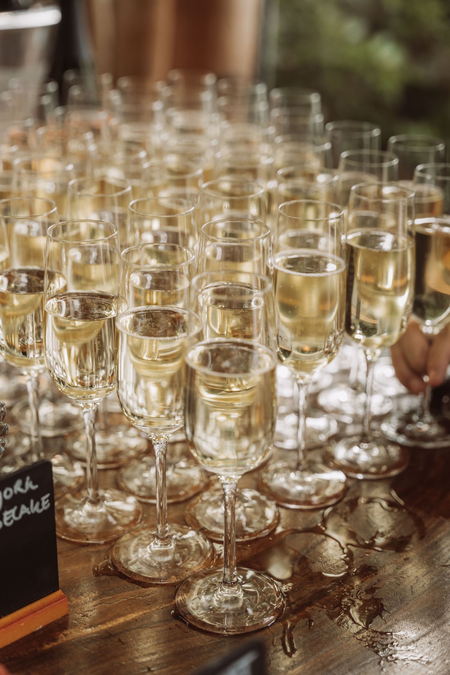 Multiple champagne flutes filled with sparkling wine arranged on a wooden table at an elegant event.