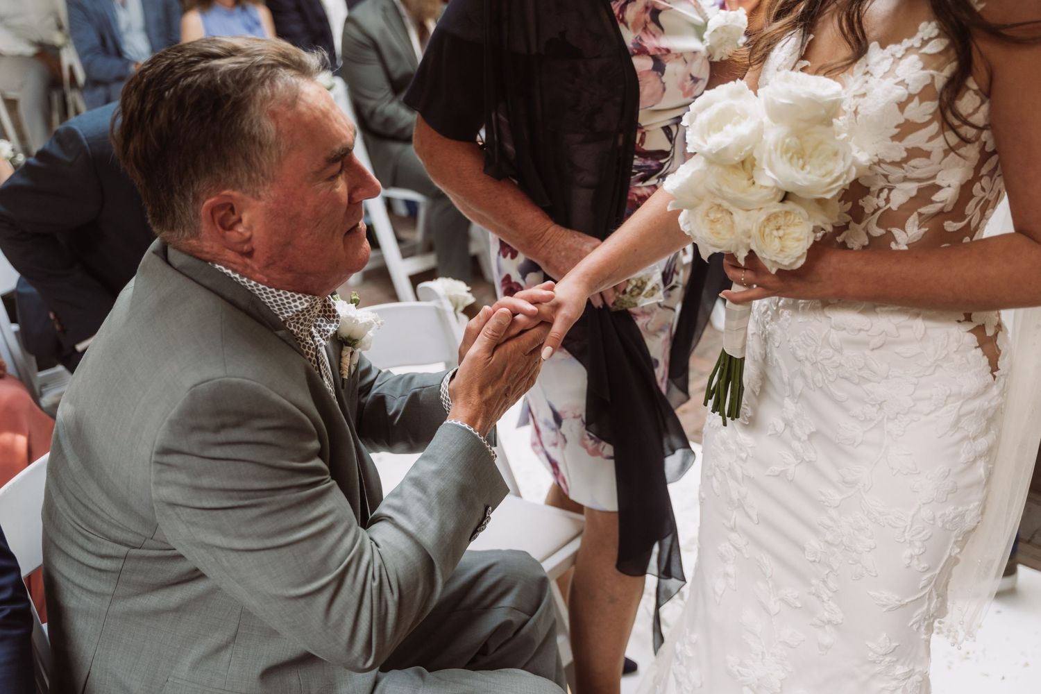 A groom kisses his bride's hand during an elegant wedding reception while guests look on.