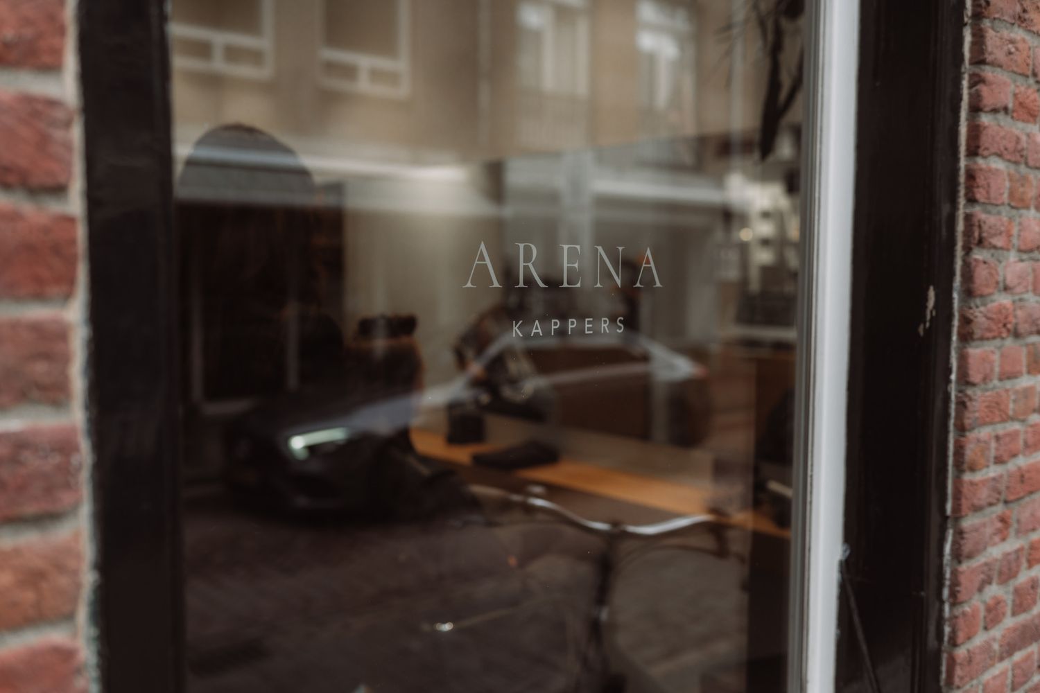 Frosted glass window with 'ARENA' text etched on it, reflecting interior wooden furniture and brick exterior.