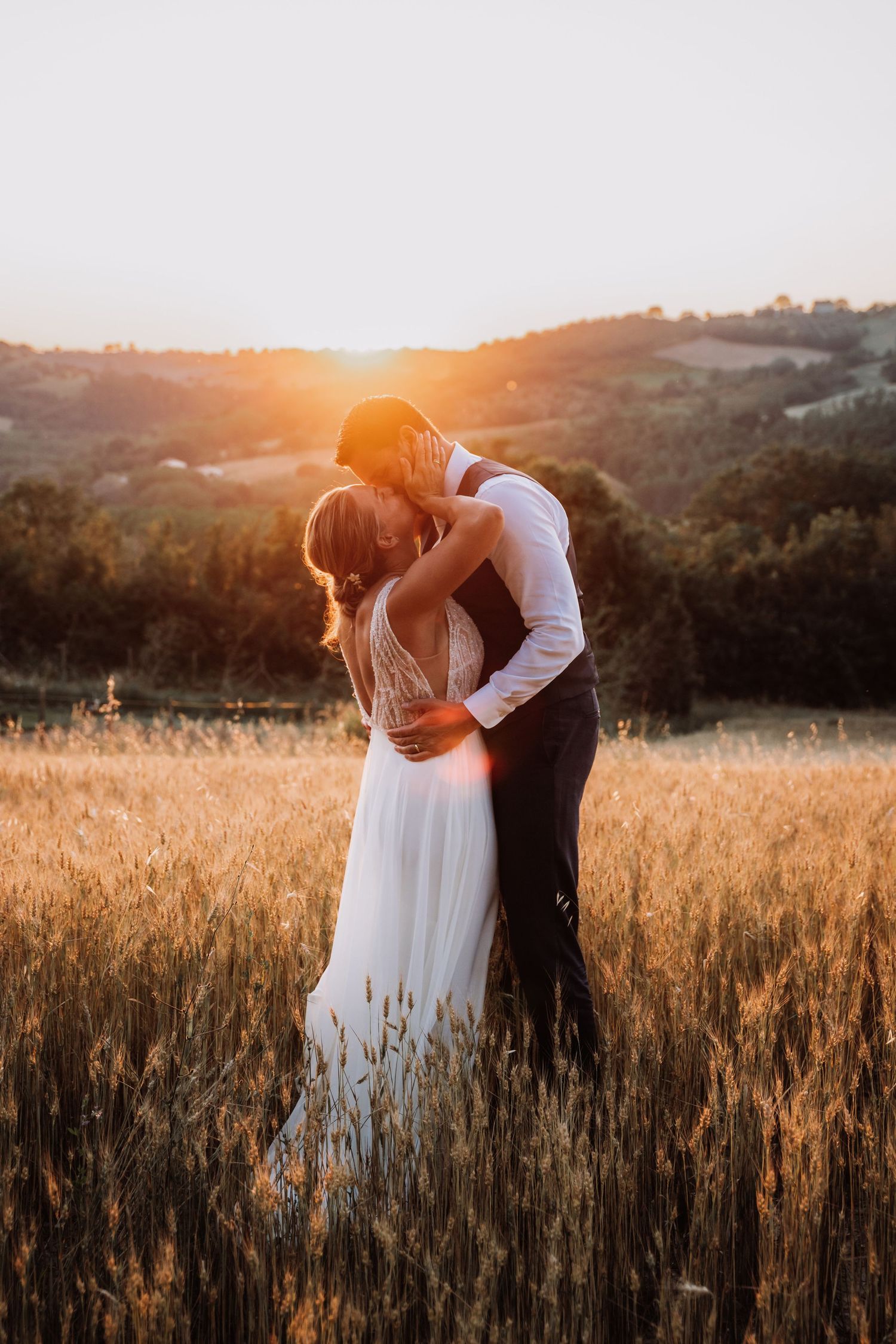 A romantic couple embraces in a golden wheat field at sunset creating a dreamy silhouette against the warm sky.