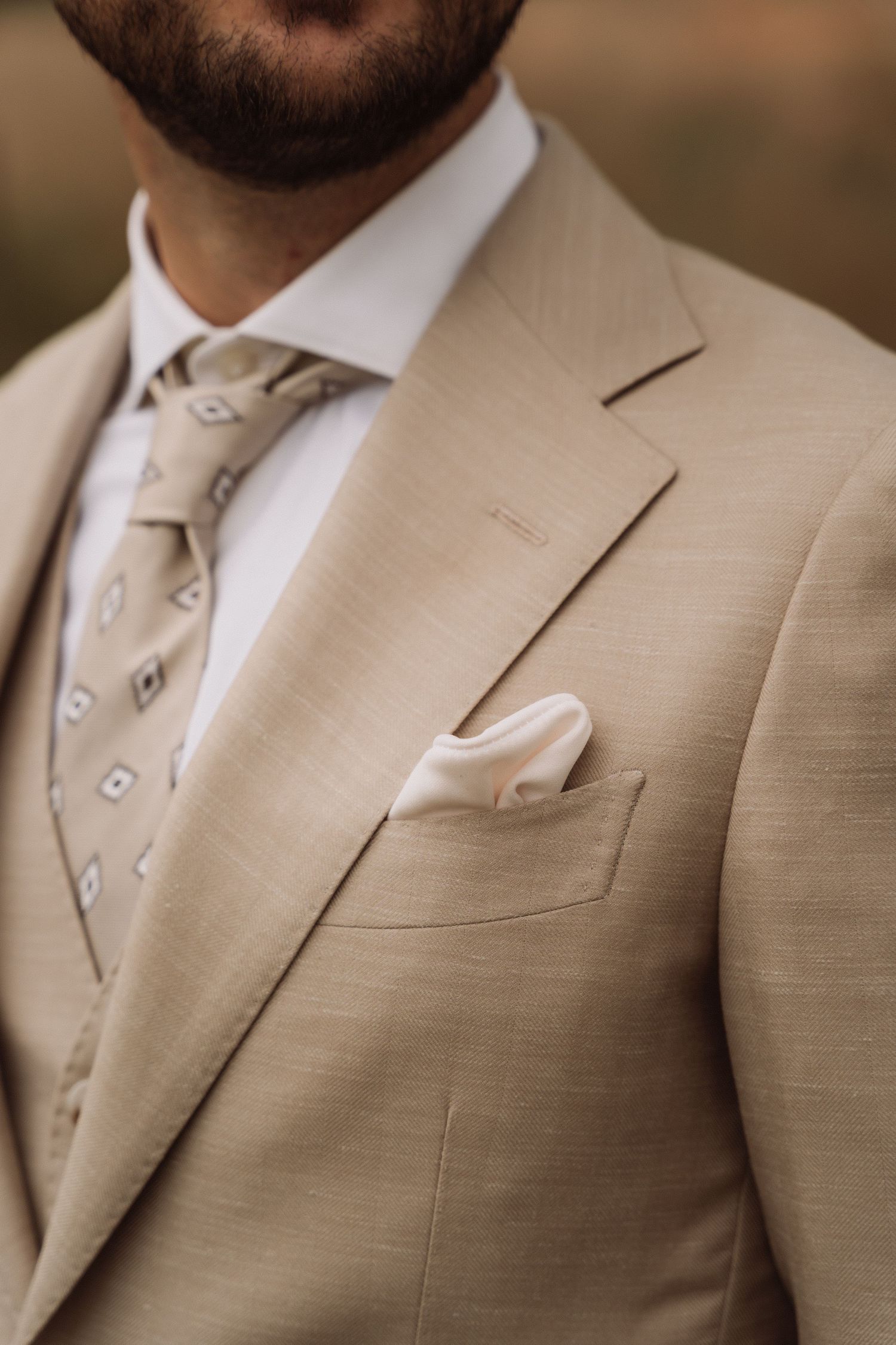 Close-up details of a tan wedding suit with matching tie and white dress shirt.
