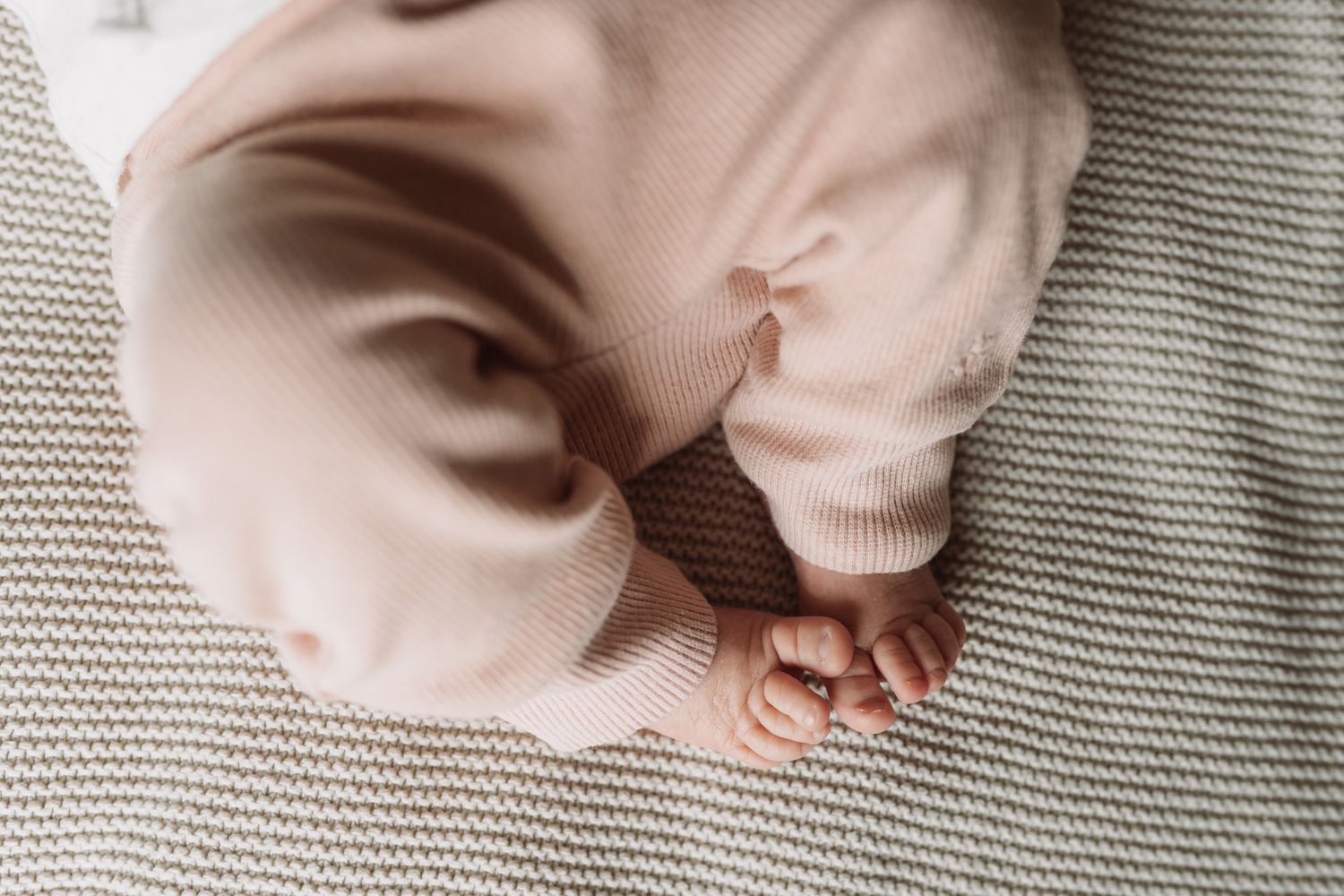 Close-up of tiny baby feet in soft pink clothing on textured gray fabric.