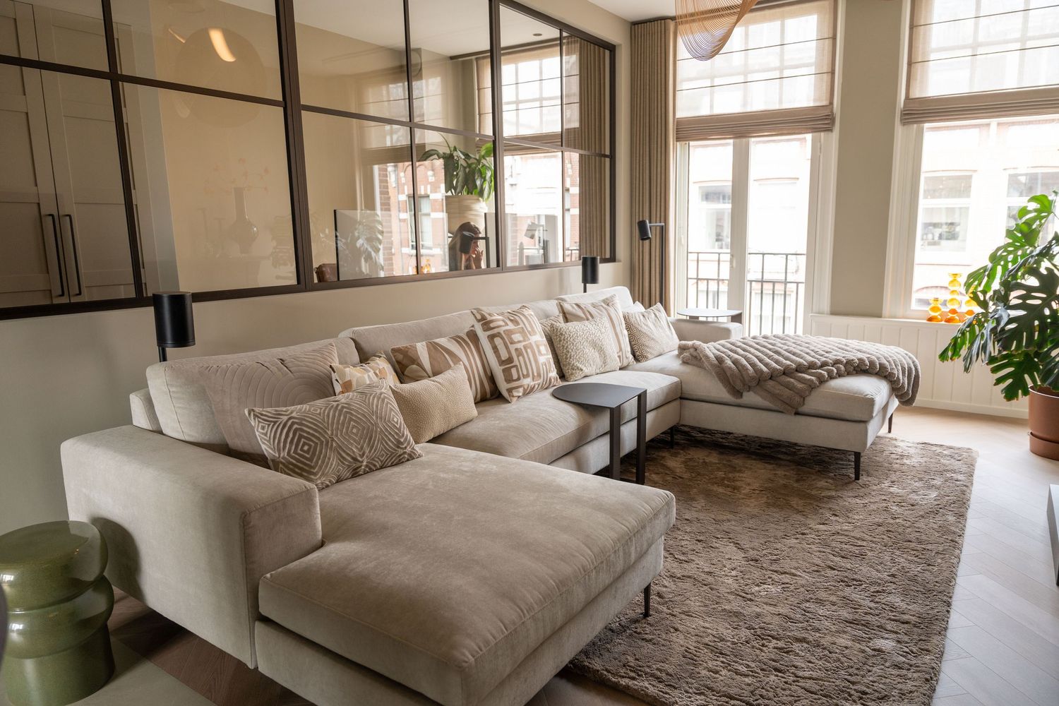 Modern living room with plush beige sectional sofa, large windows, and contemporary decor on a textured area rug.