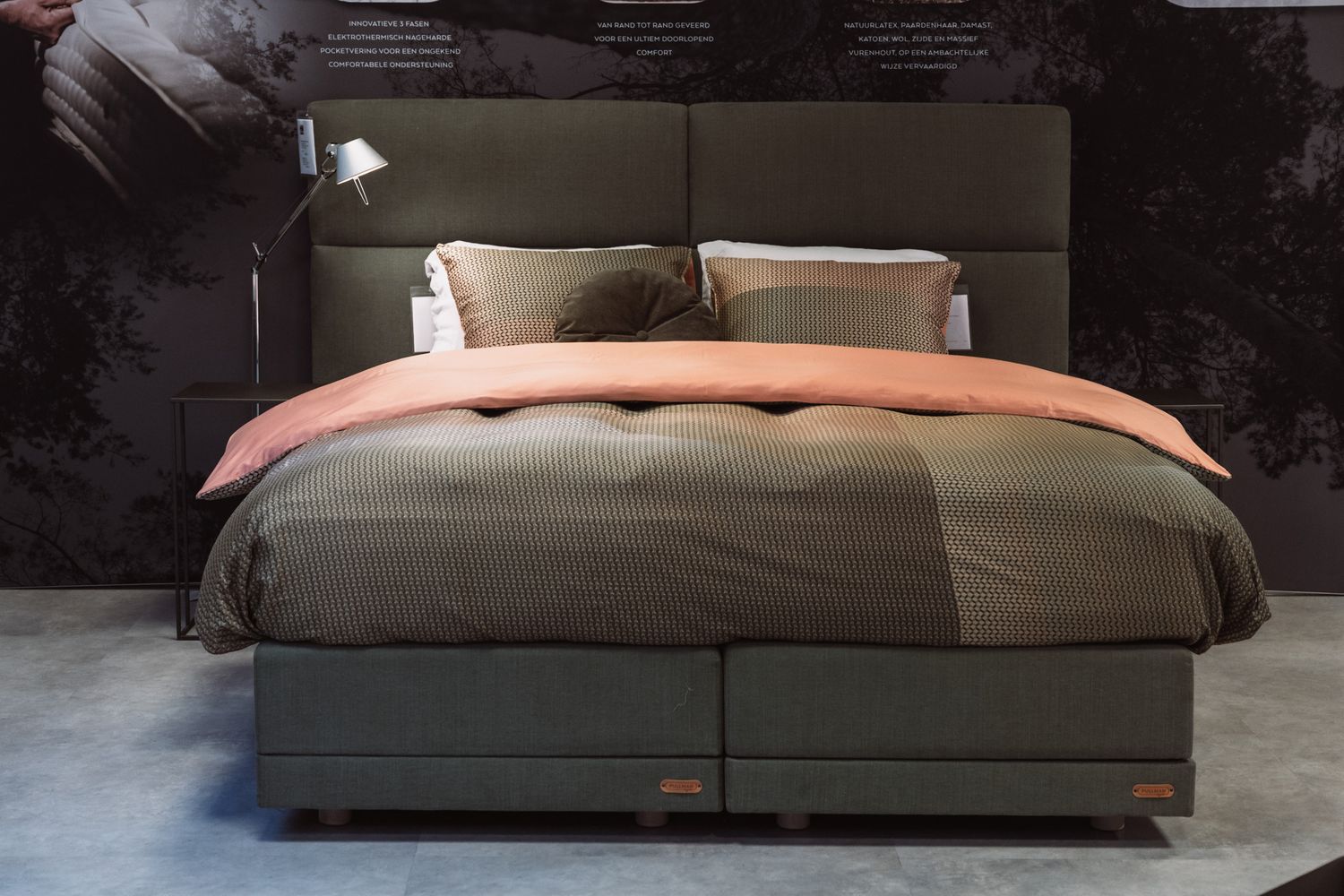 Modern bed with olive green bedding and salmon pink duvet cover on gray platform frame in dark room setting.
