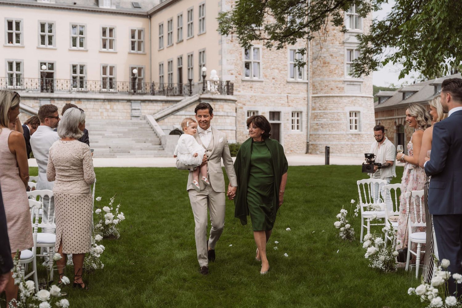 Wedding guests enjoy an outdoor garden reception with white chairs and tables set up on a manicured lawn.