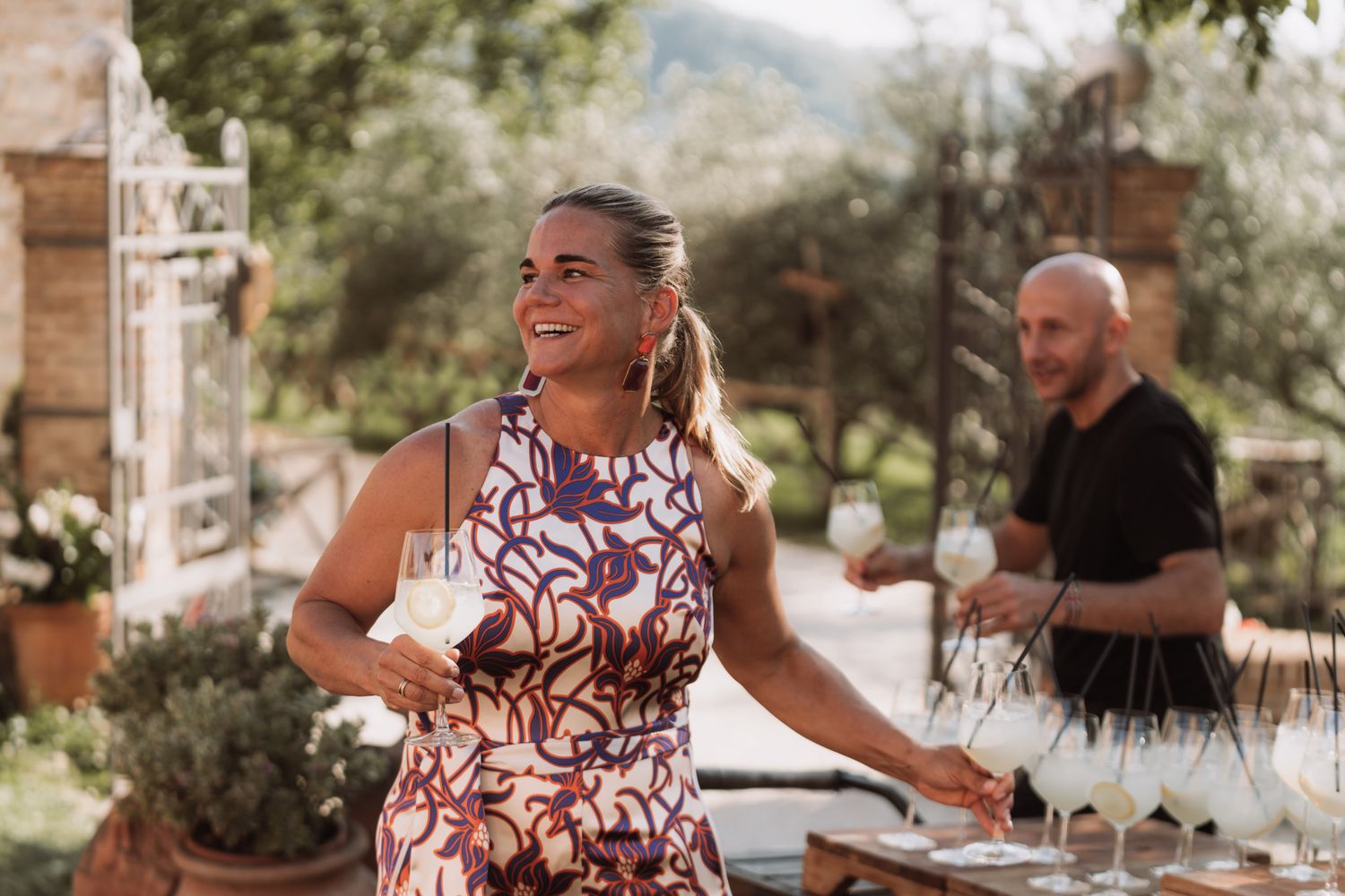 A group of people enjoy an outdoor dining experience at a rustic venue with stone columns and natural lighting.
