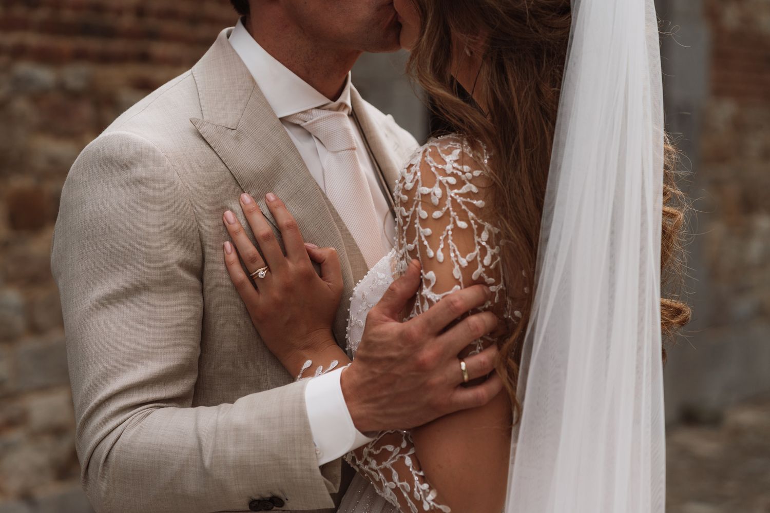 Romantic close-up of a couple in wedding attire against a brick wall.