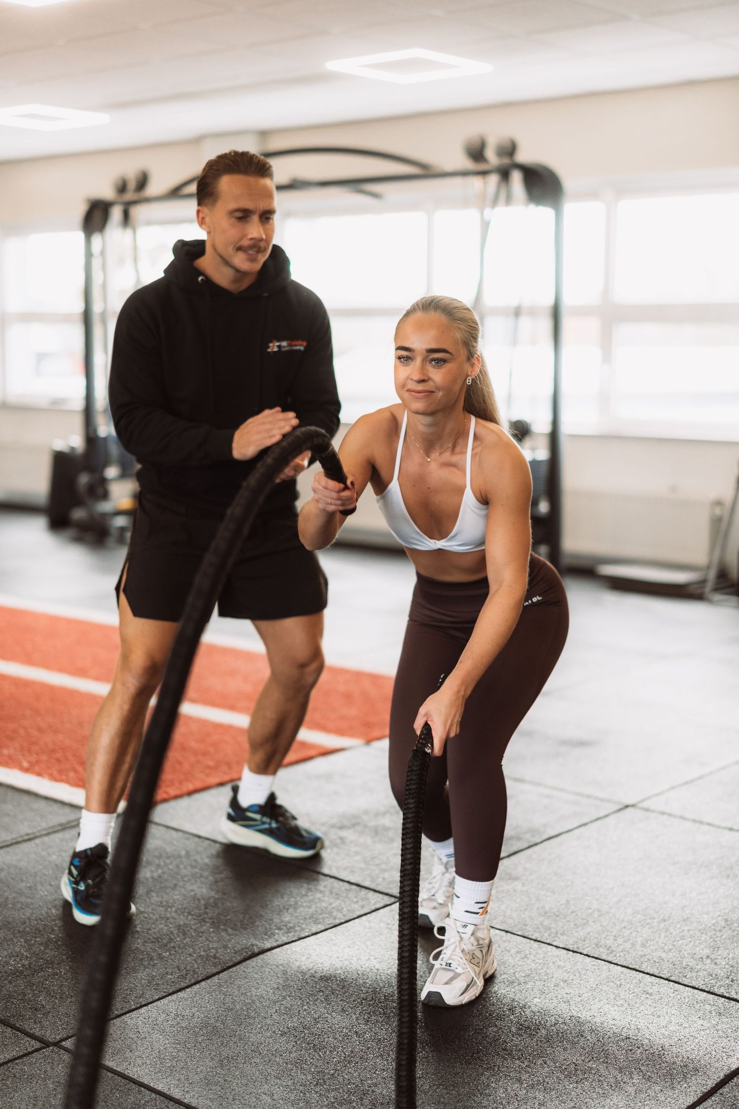 Athletic person performing lunges with trainer guidance during workout session in bright fitness studio.