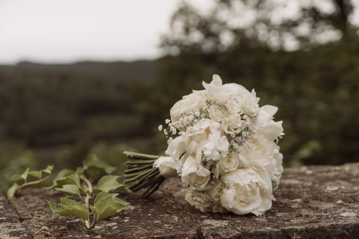 A delicate white floral bouquet rests on a rustic wooden surface in natural outdoor lighting.
