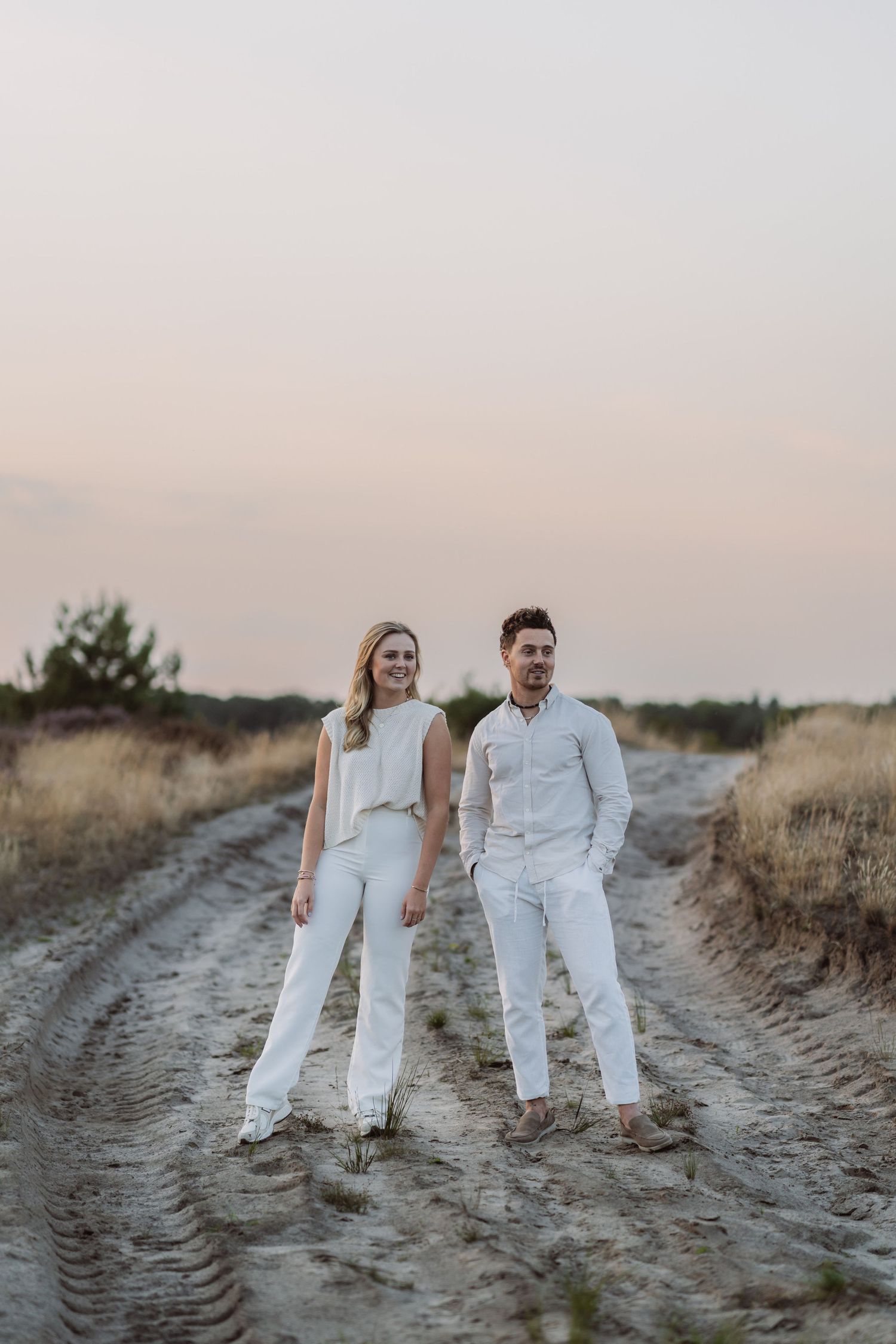 Couple in matching white outfits standing on a dirt path at dusk.