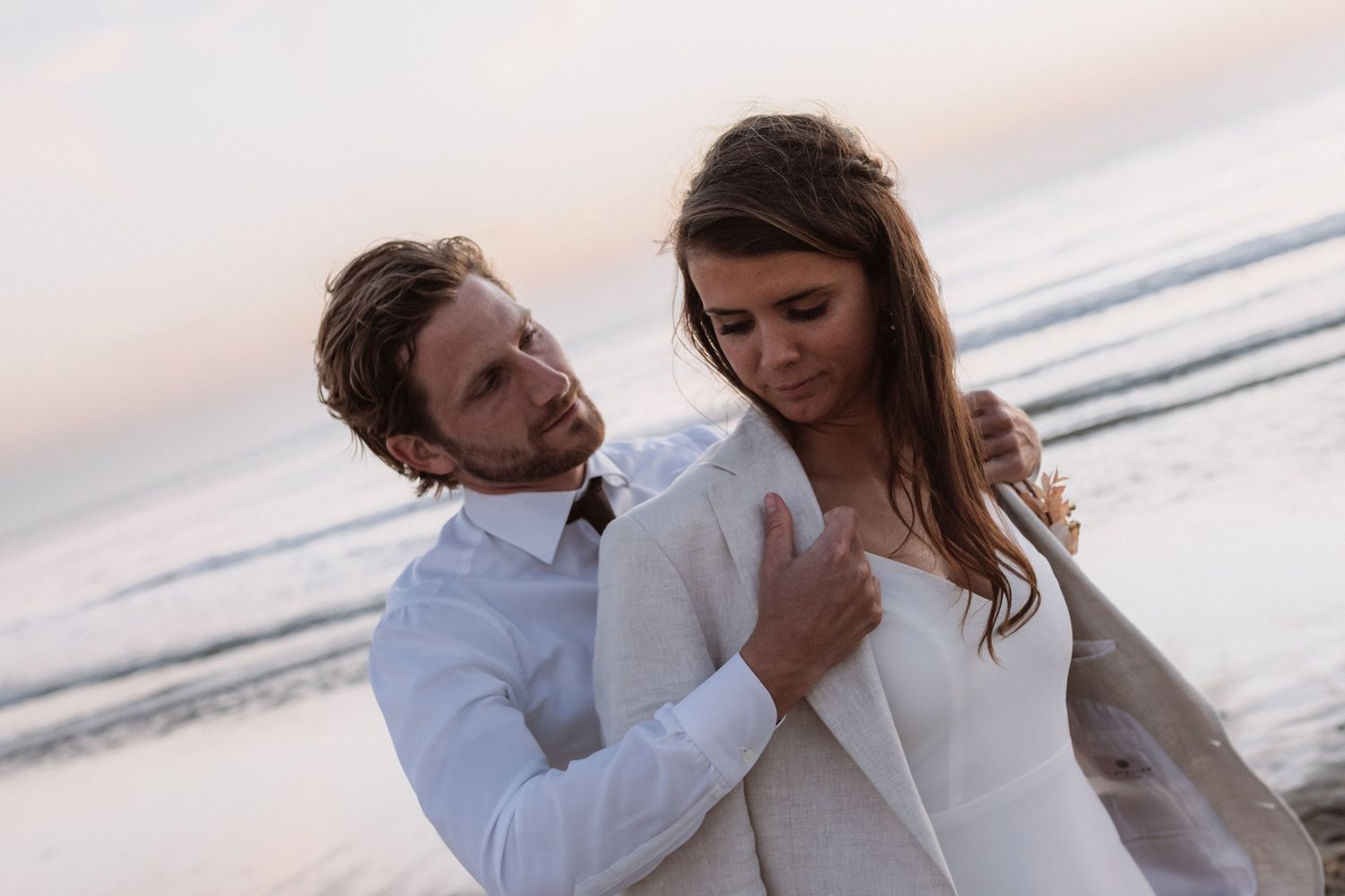 Romantic couple in white embracing on beach during sunset.