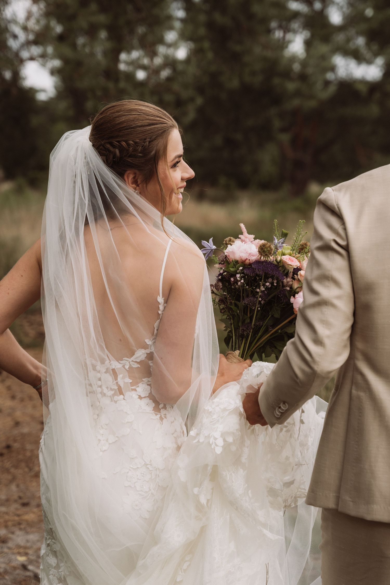 A couple in wedding attire shares a playful moment outdoors with the bride's veil flowing in the wind.