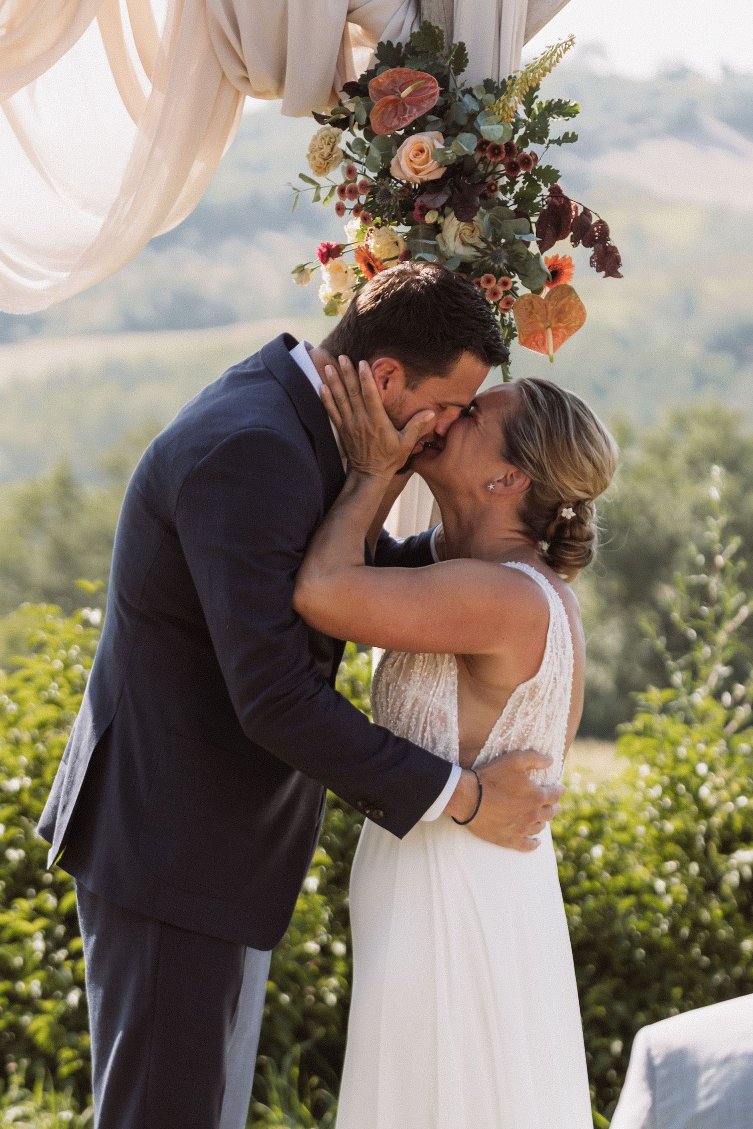 A romantic first kiss between newlyweds at an outdoor wedding ceremony with mountains in the background.
