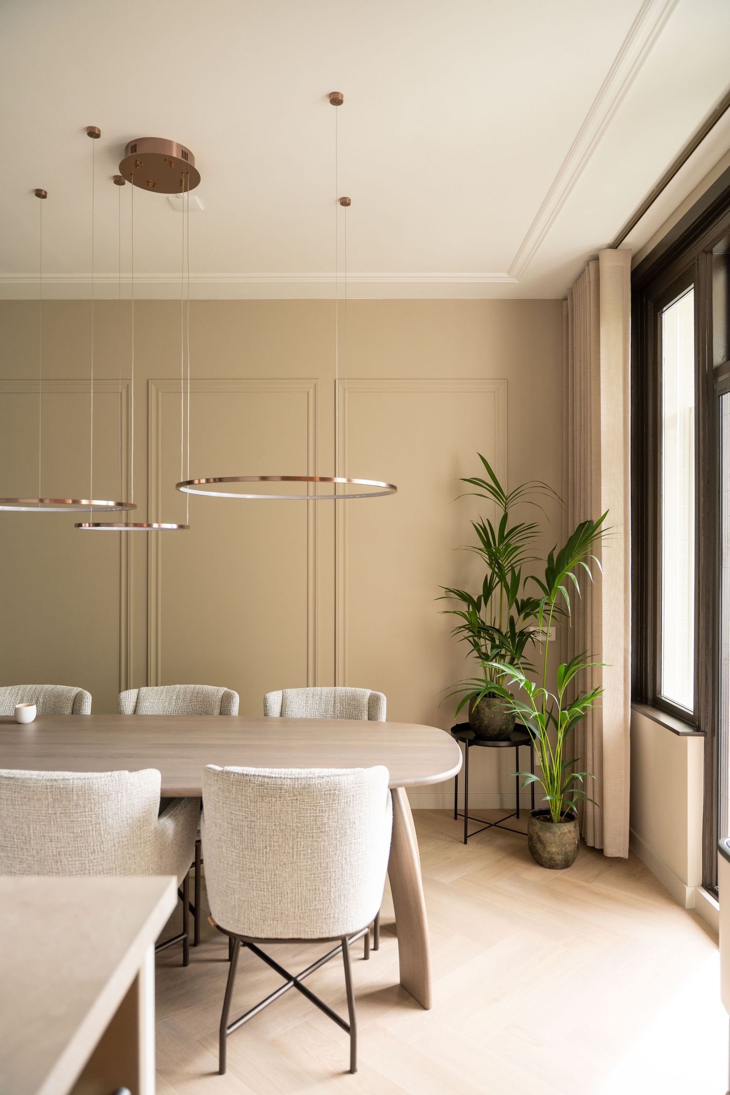 Modern dining room with beige walls, upholstered chairs, oval table and contemporary pendant lighting fixtures.