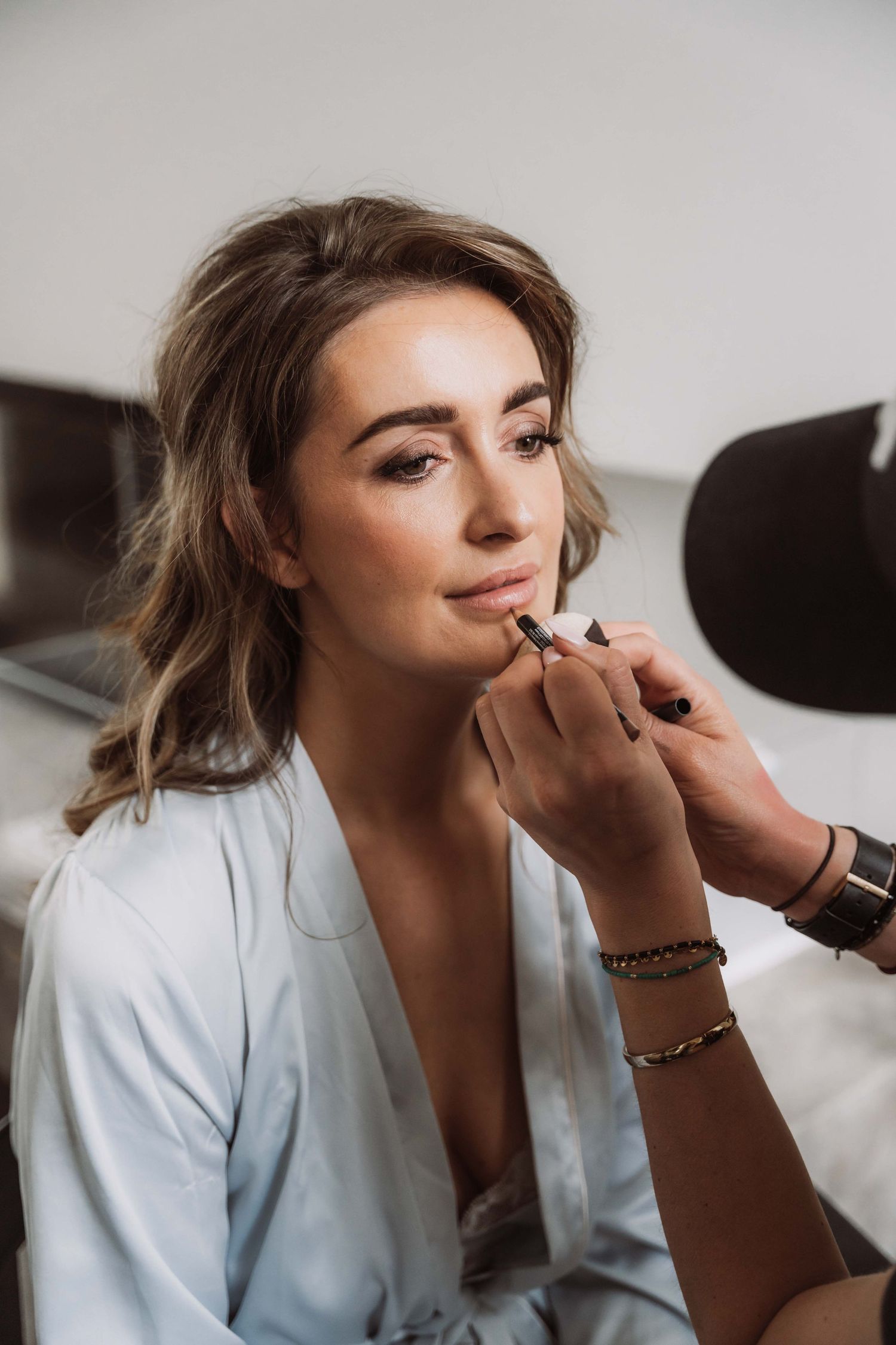 A makeup artist applies lipstick to a model wearing a white blazer in a professional beauty session.