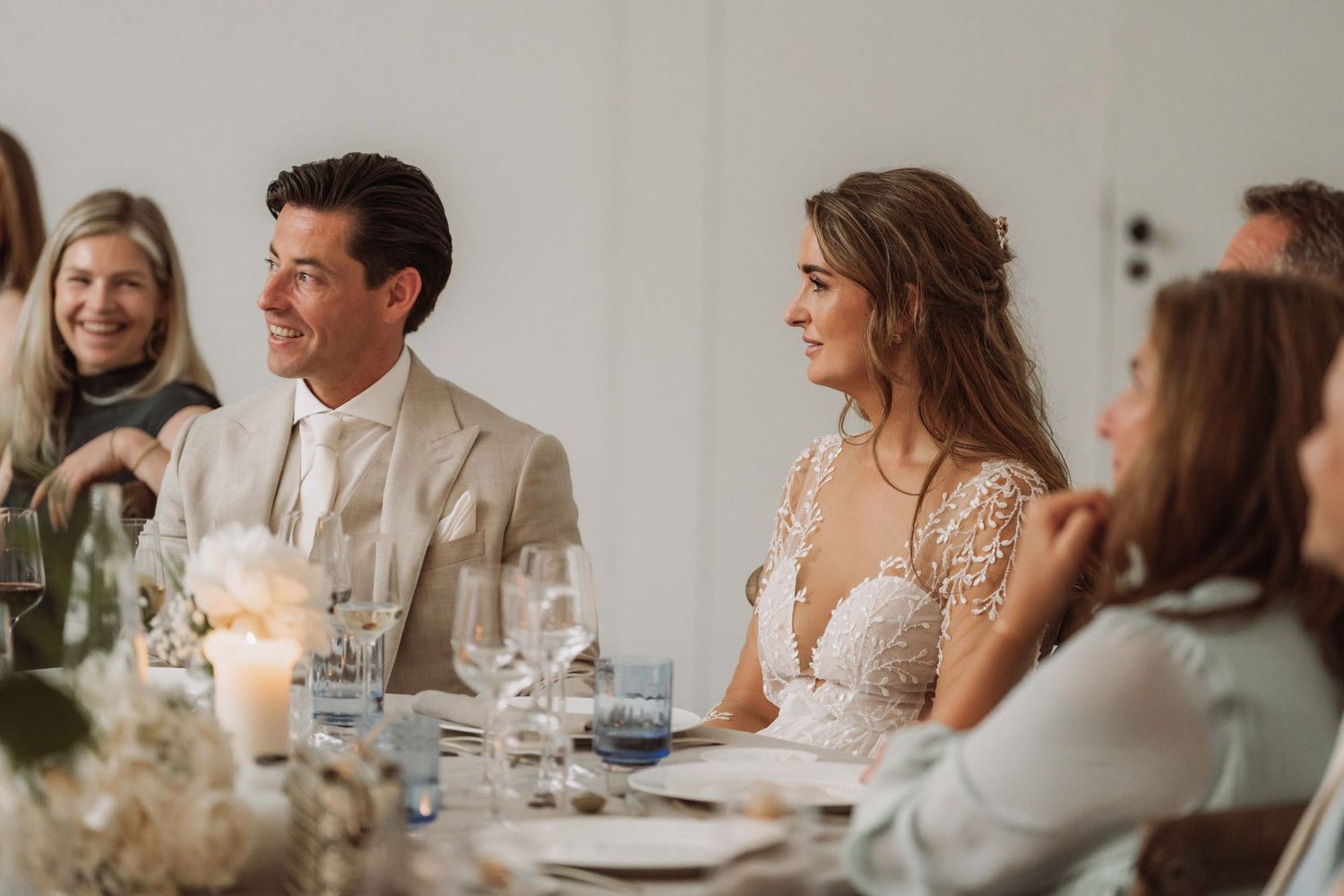 Wedding guests seated at a long table engage in lively conversation during an elegant reception dinner.
