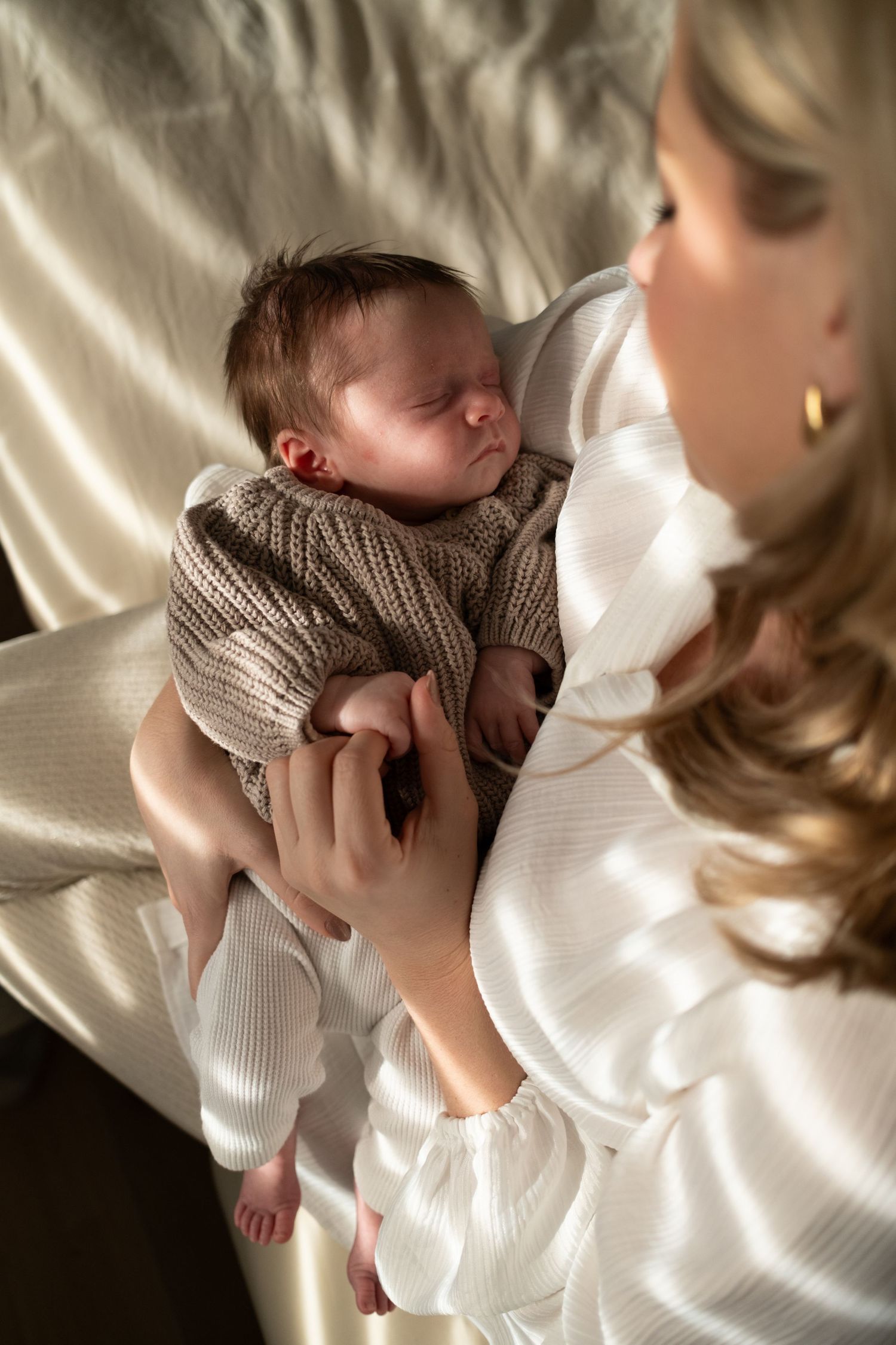 Tender moment between parent and newborn baby in soft natural window light.