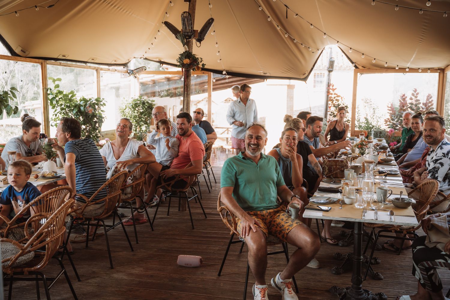 A large group of people seated under a white tent canopy at an outdoor event or gathering.